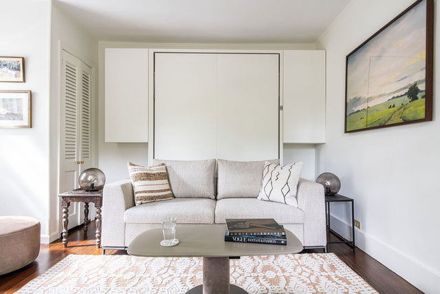 Tonale motorized sofa wall bed in compact living room with neutral sofa, wall storage, and folding queen bed closed against the wall.