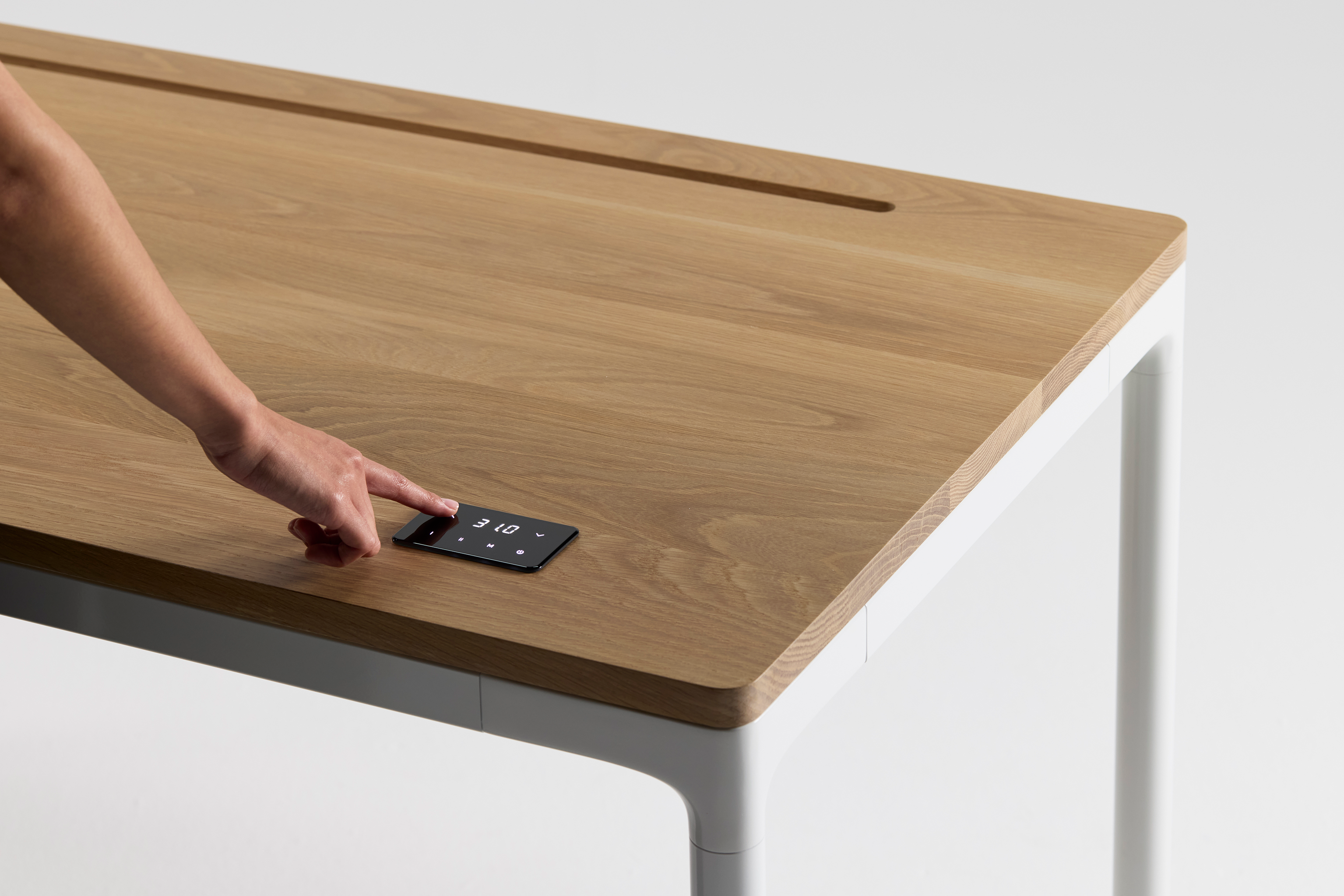 User adjusting the digital height control on a solid wood eFloat Quattro sit/stand desk with integrated cable slot and rounded white legs.