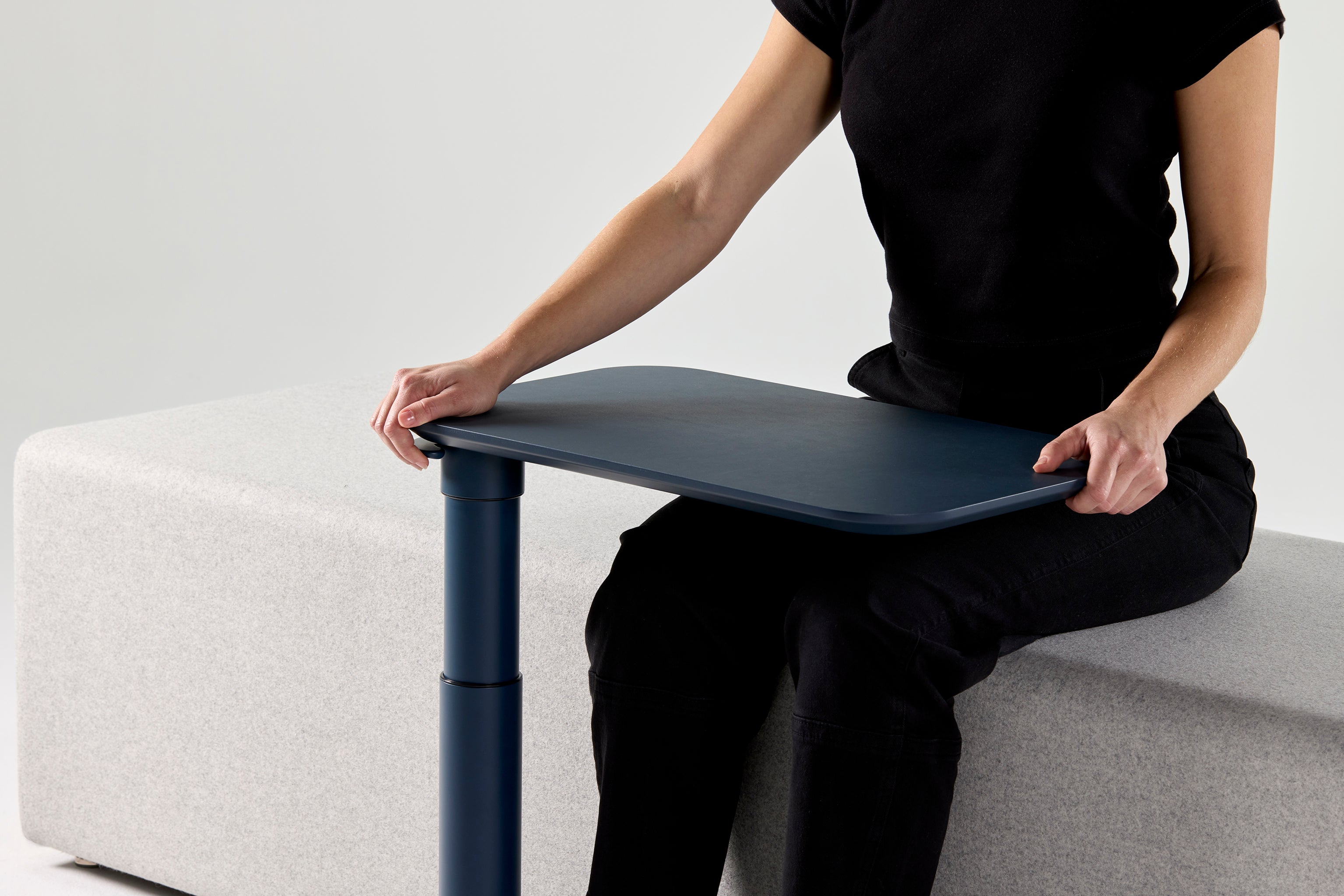 User adjusting the height of the black Float Micro table while seated, showcasing ergonomic mobility.
