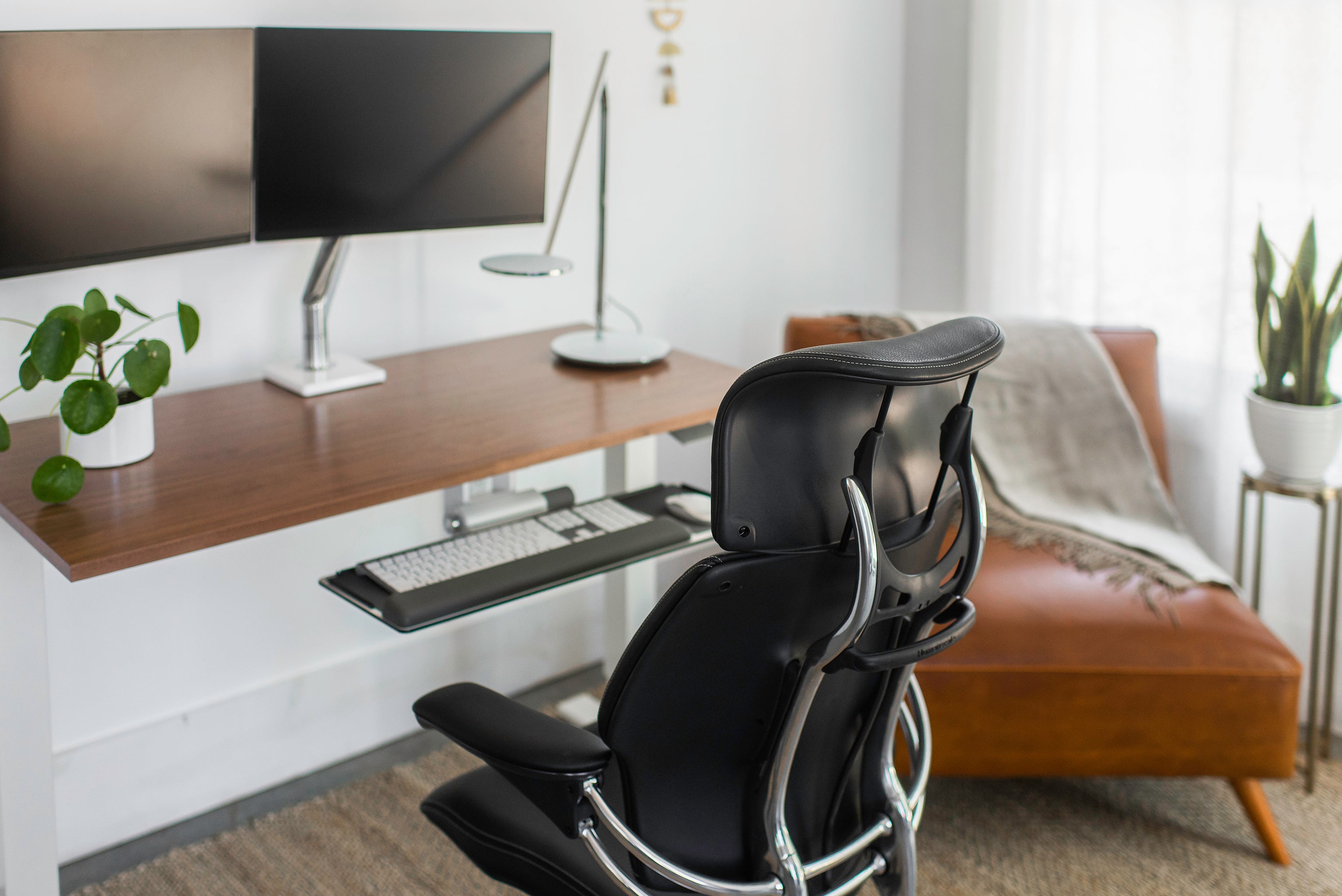 Rear view of black Freedom Headrest chair in a modern home office with dual monitors and a walnut sit-stand desk.