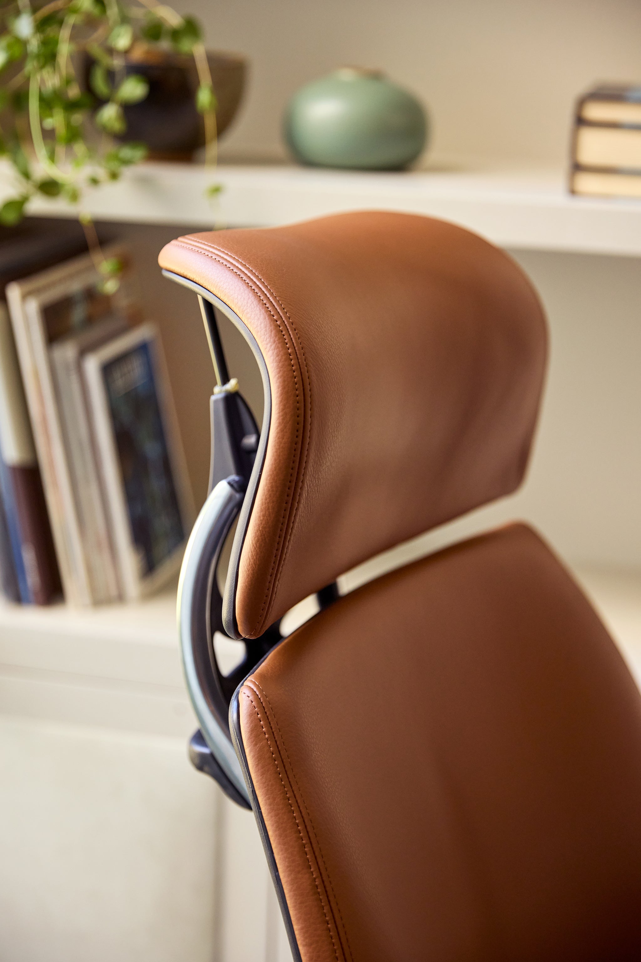 Close-up detail of the Freedom Headrest ergonomic chair showing tan leather upholstery and curved headrest stitching.