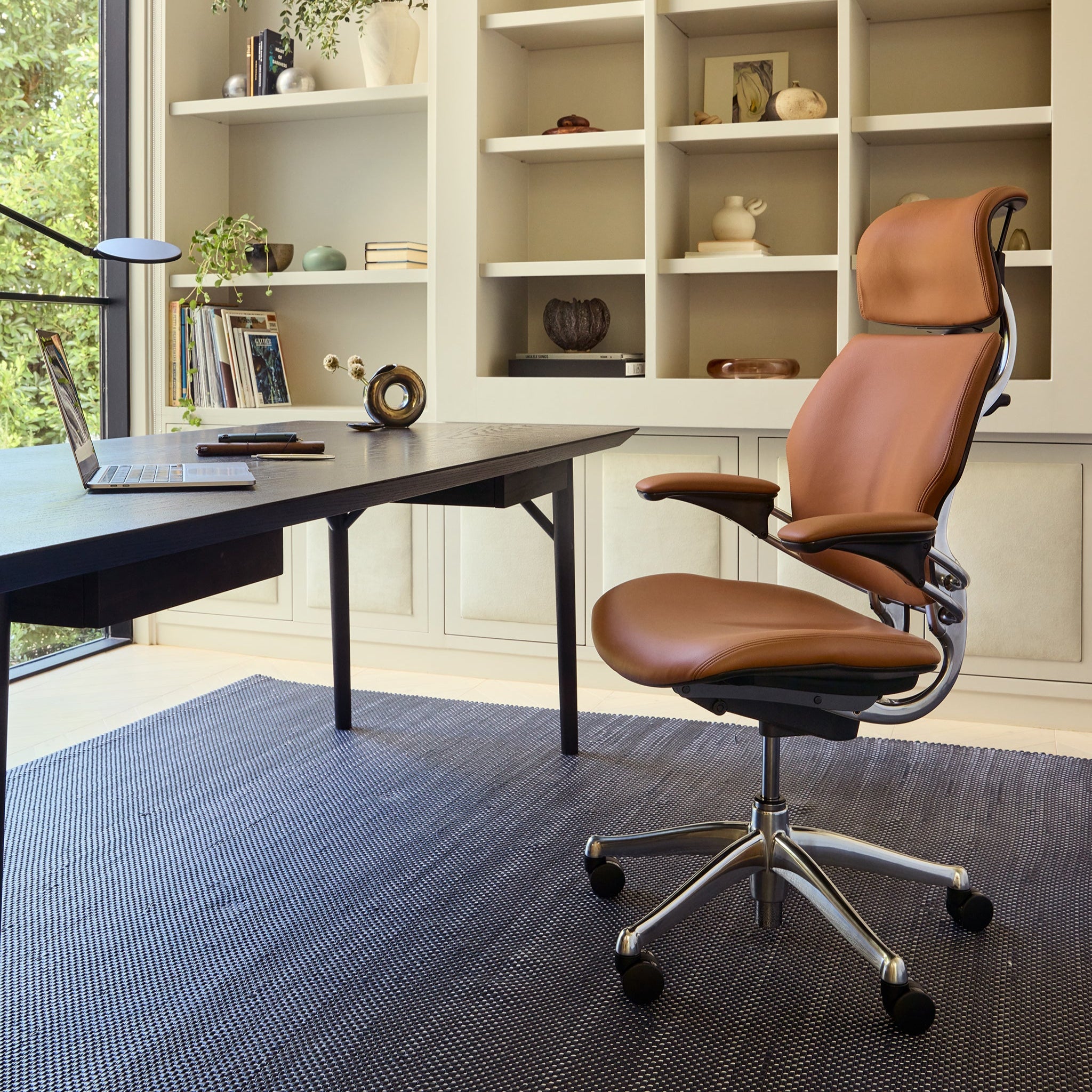 Full view of the Freedom Headrest in tan leather beside a modern desk in a home office with built-in shelving and natural light.