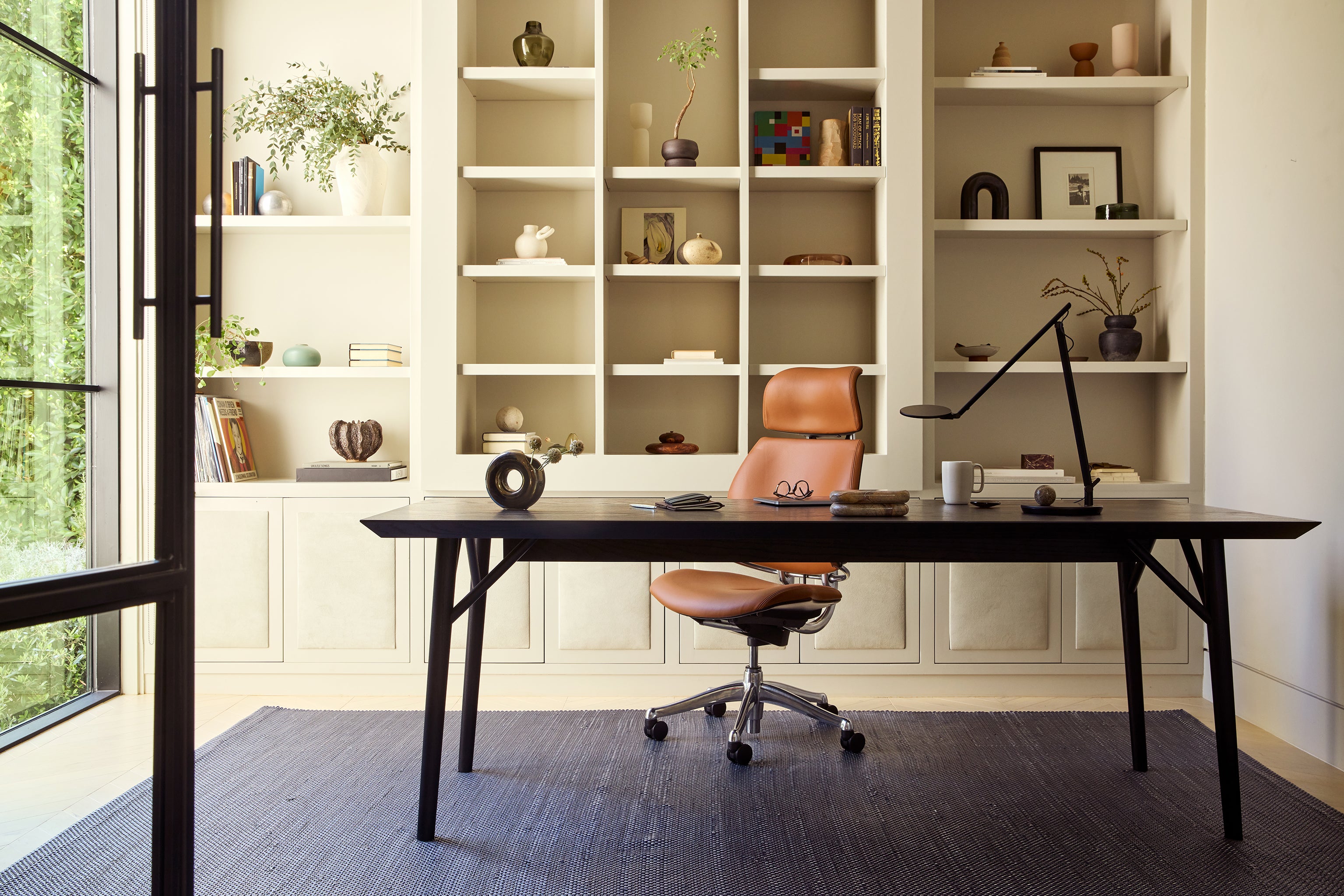 Freedom Headrest in tan leather positioned at a dark wood desk in a curated home office and library setting.