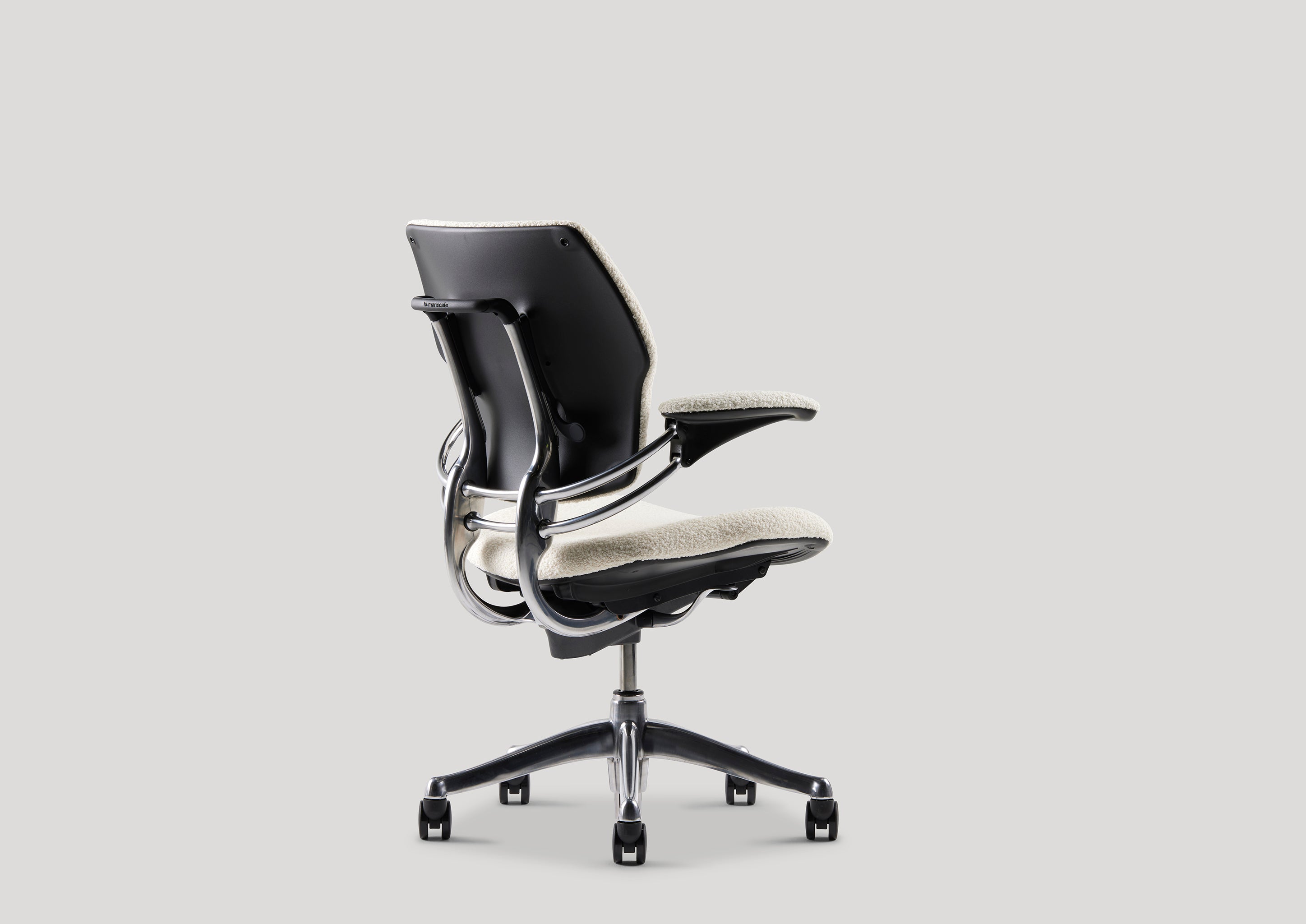 Three-quarter rear view of Freedom Task Chair showing black shell and ivory padding over ergonomic frame with caster base.