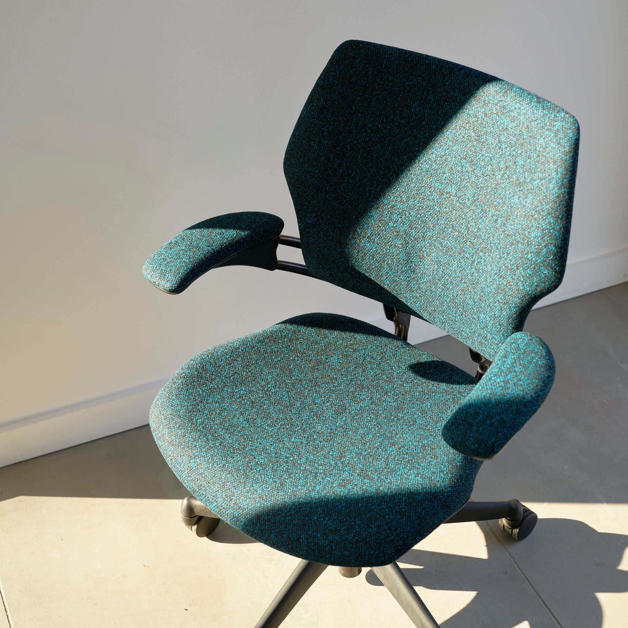 Freedom Task Chair in teal upholstery, illuminated by sunlight in a minimalist room with tiled flooring.