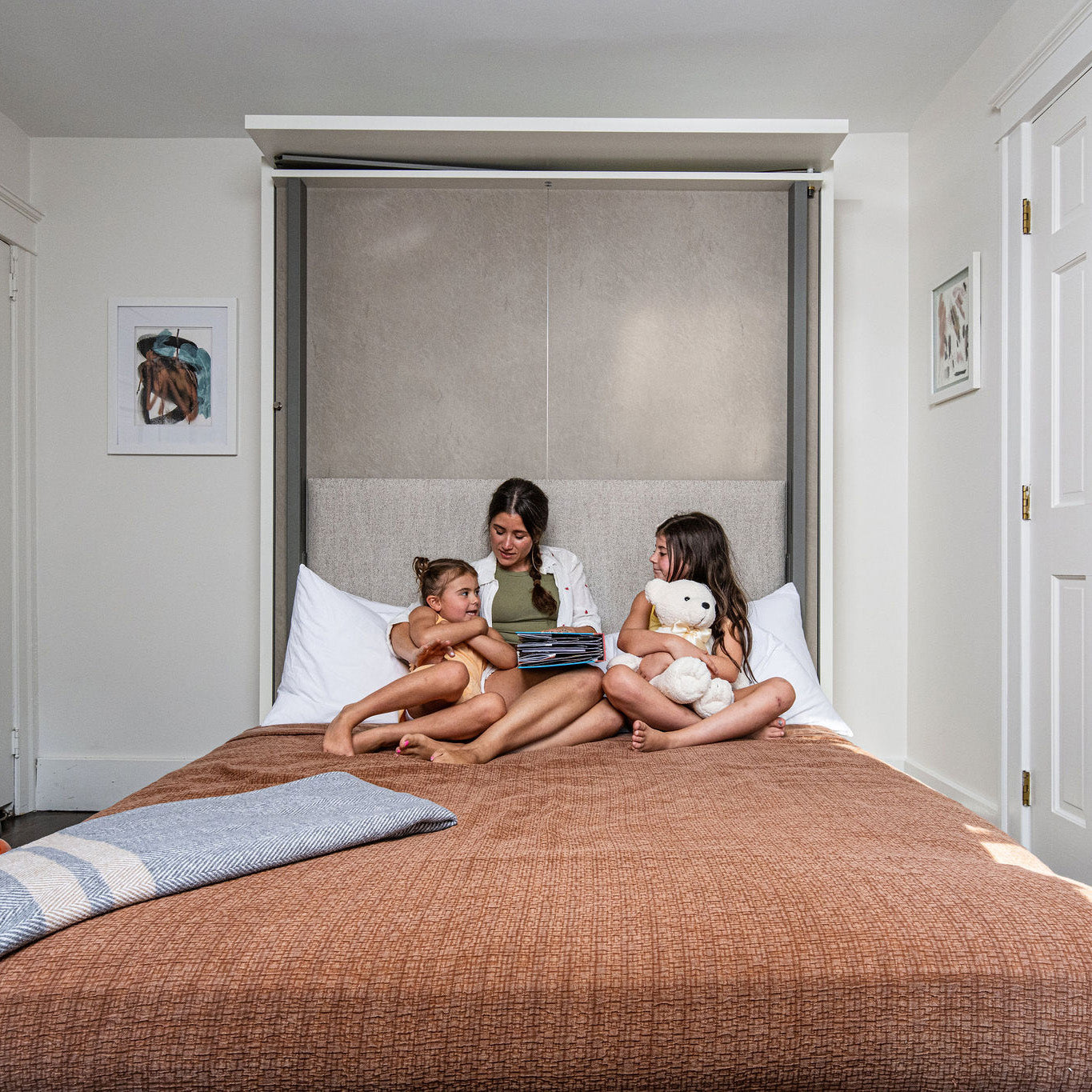 Mother reading to two children on the fully open LGM wall bed, illustrating family-friendly multifunctional furniture ideal for compact kids’ bedrooms and shared spaces.