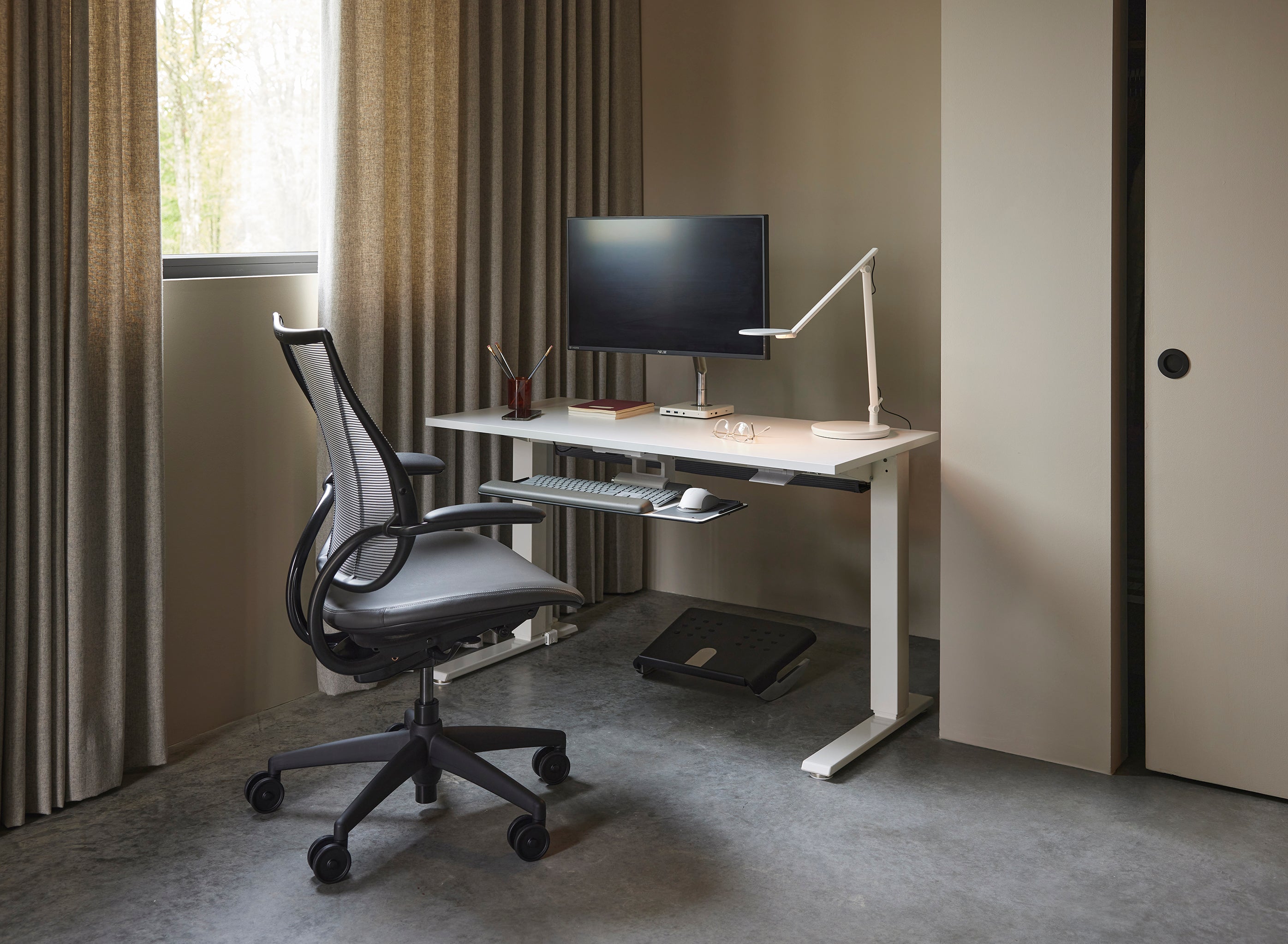 Liberty Task Chair in graphite mesh and cushion at a standing desk workstation with monitor and task light.