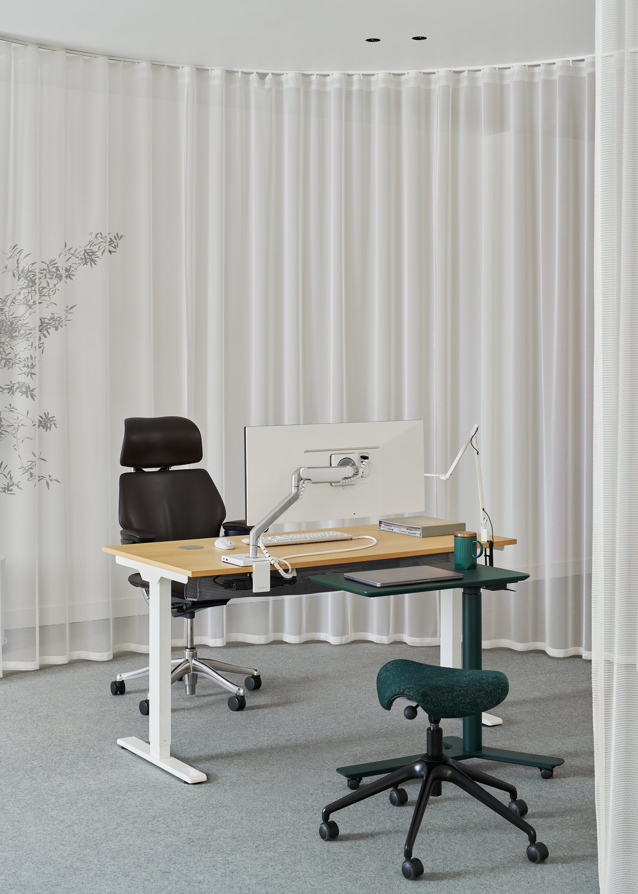 Pony saddle chair in green fabric at a height-adjustable workstation in an office, paired with a black executive task chair.