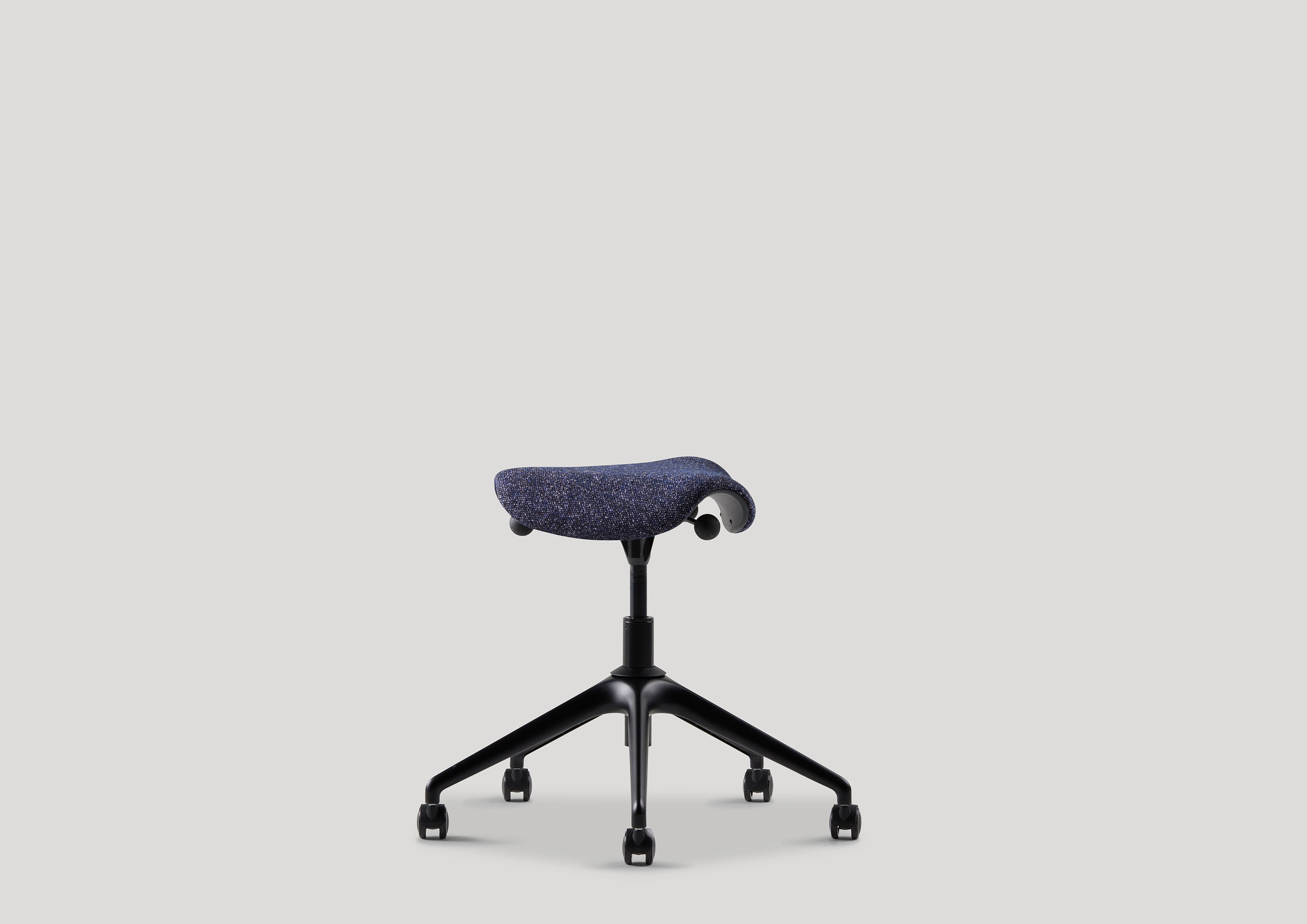 Navy Kvadrat-upholstered Pony stool with ergonomic saddle seat and black base, shown in angled profile.