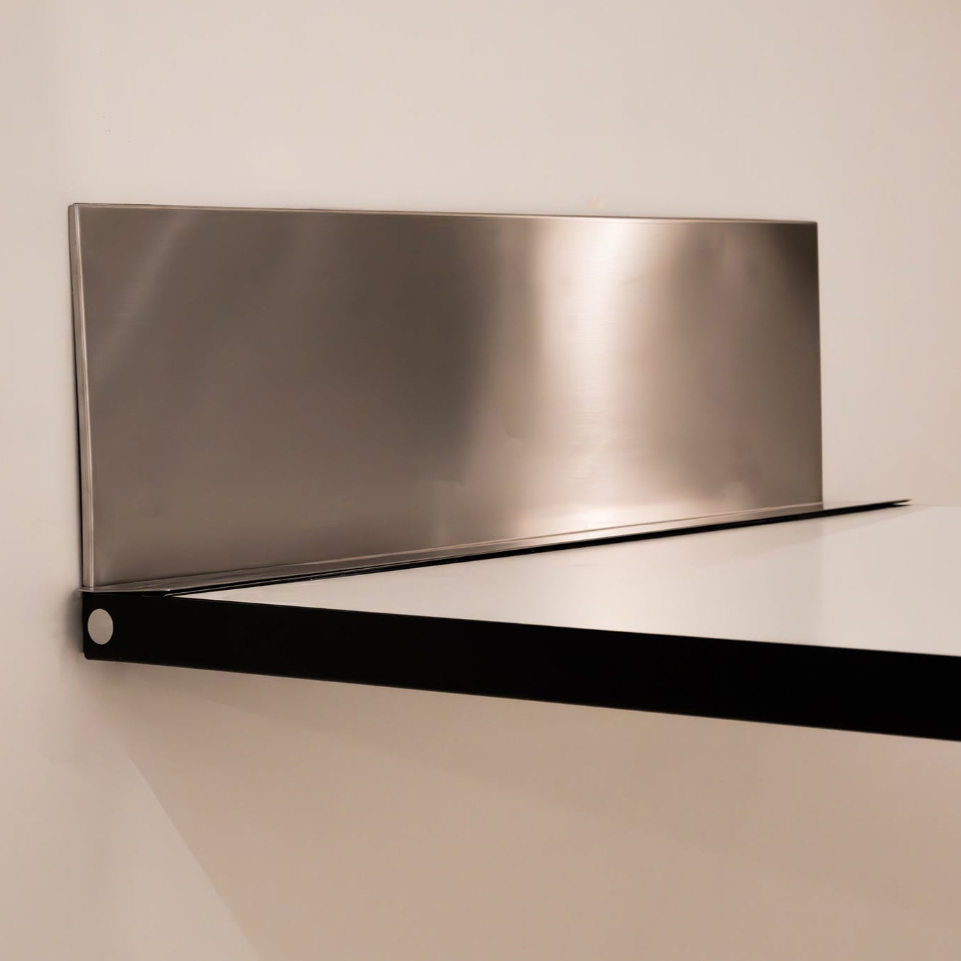 Close-up of Specchio table’s brushed metal backplate and black folding frame.