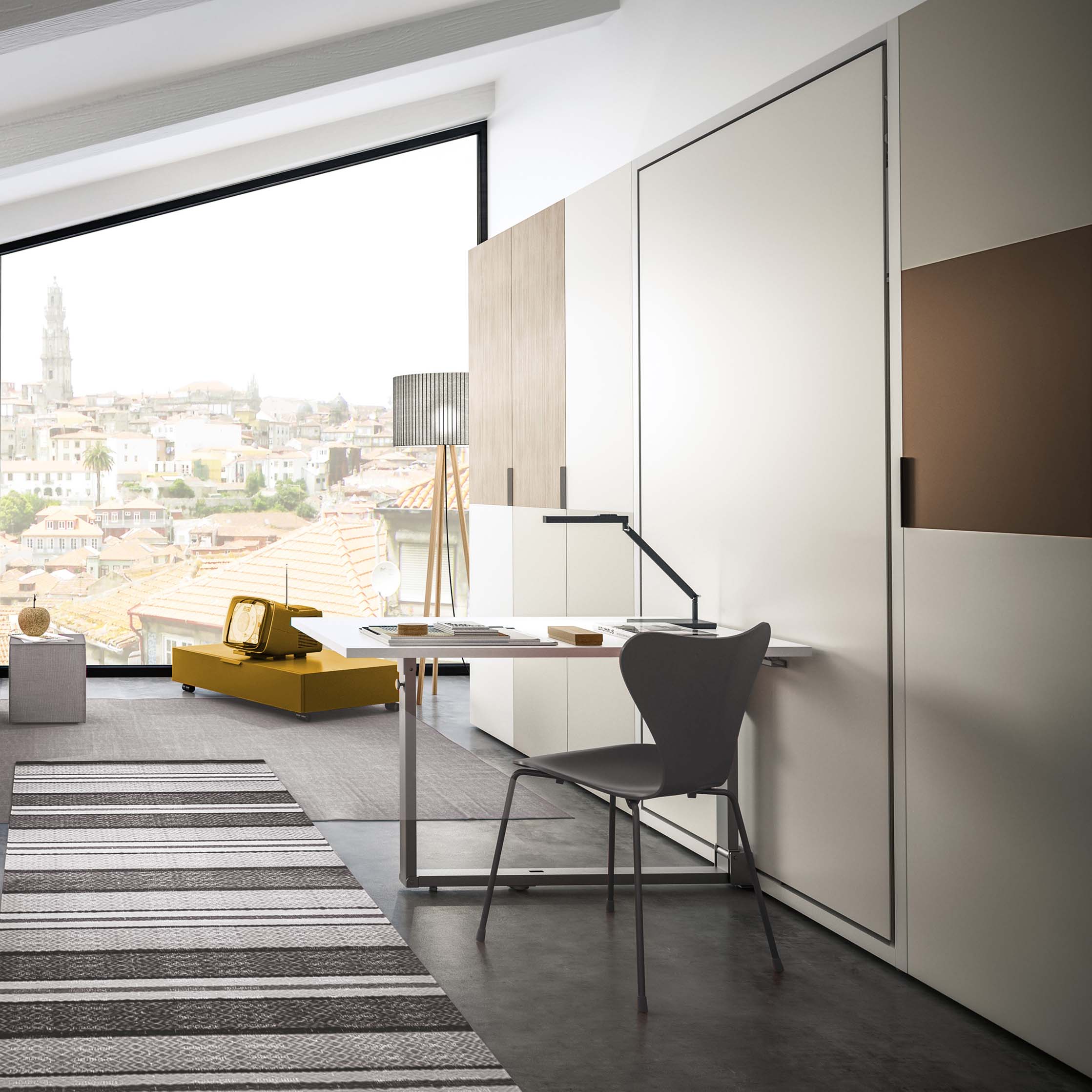 Altea Work wall bed with integrated desk in a modern loft-style room, showcasing a space-saving home office setup with a panoramic city view.