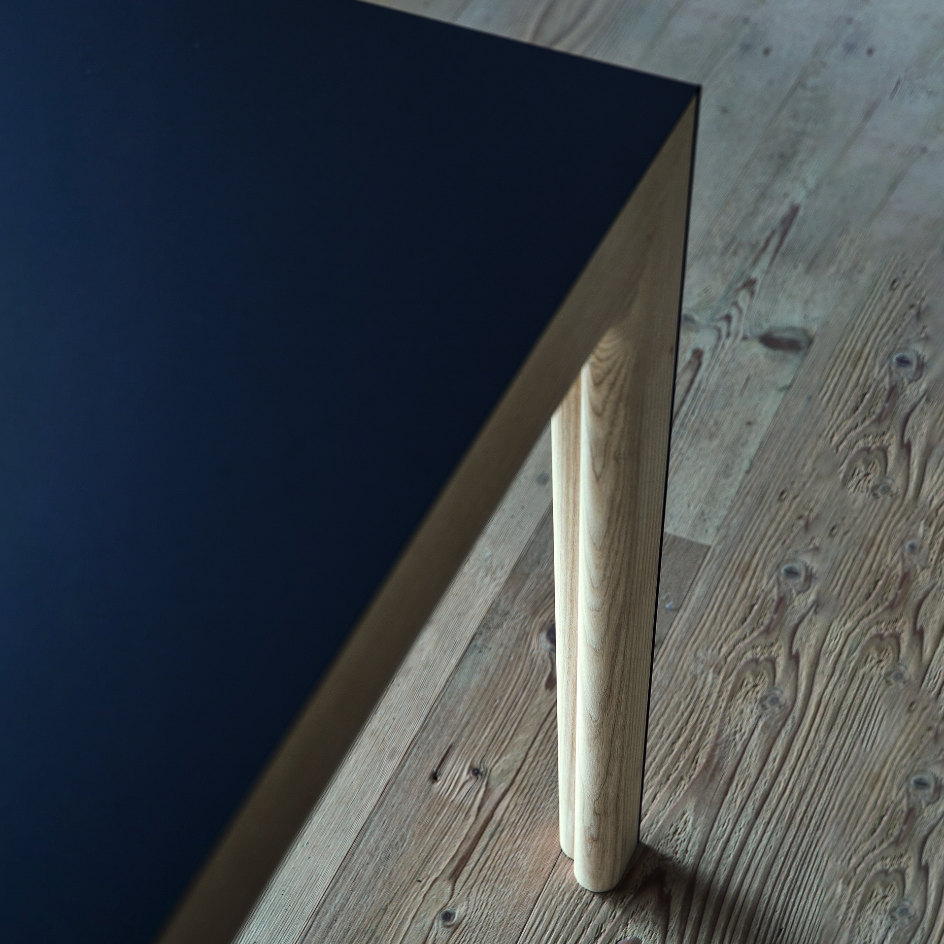 Detail view of Amalong Extension Table’s black tabletop and rounded ash wood leg, highlighting craftsmanship and material contrast.