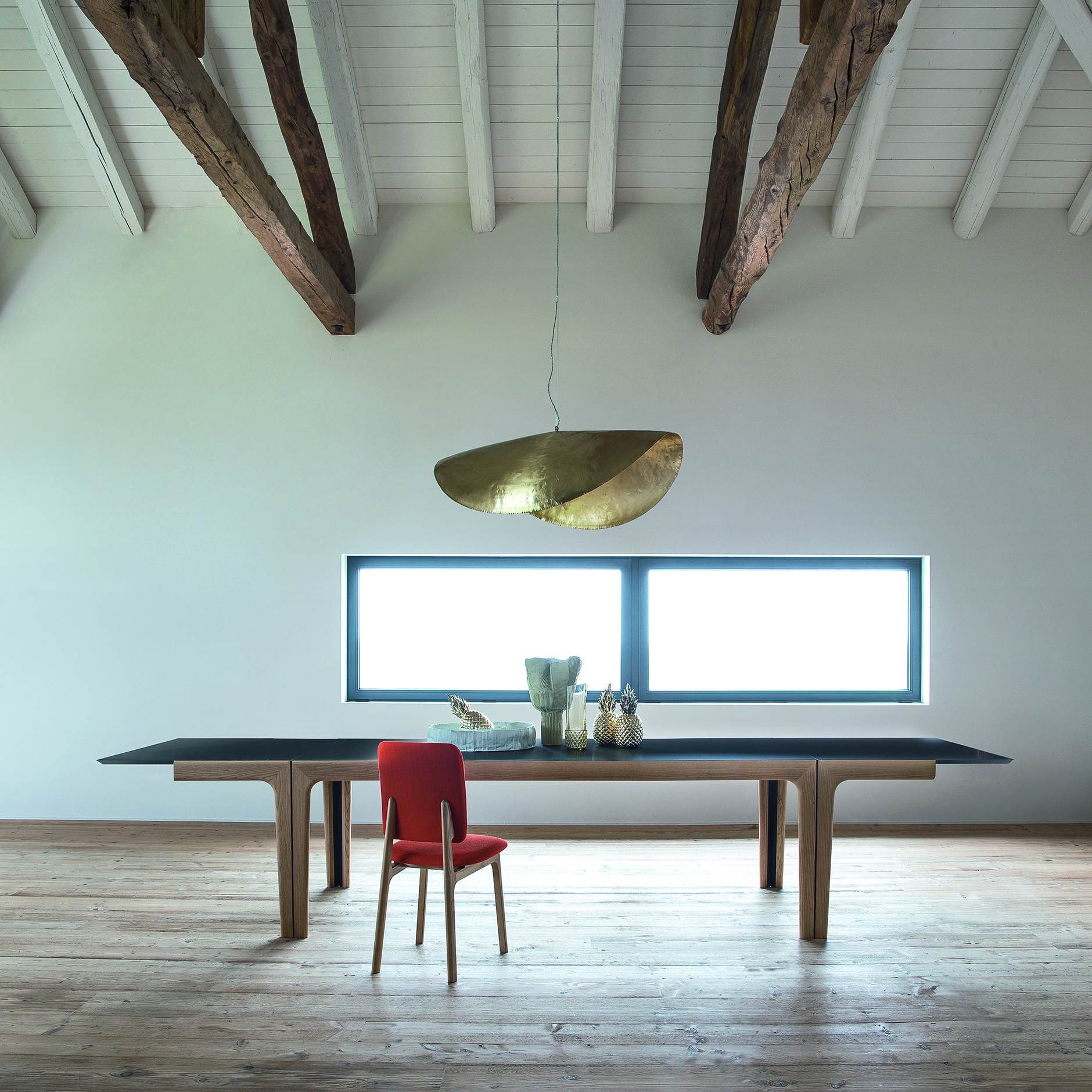 Amalong Extension Dining Table fully extended in a modern interior with wood beams, natural light, and a single red chair.