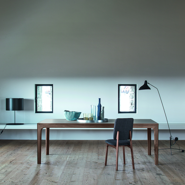 Amalong Extension Table in natural wood finish, styled with a dark upholstered chair and minimalist lighting in a bright interior.