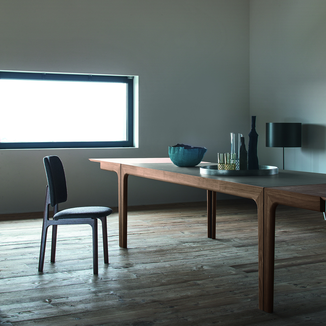 Amalong Extension Table shown partially extended in a minimalist interior with wood flooring, dark top, and sculptural styling.