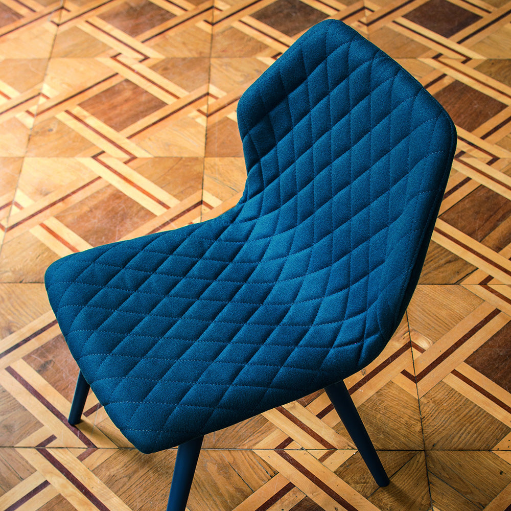 Overhead view of Ava dining chair with blue quilted upholstery, set against a geometric wood parquet floor.