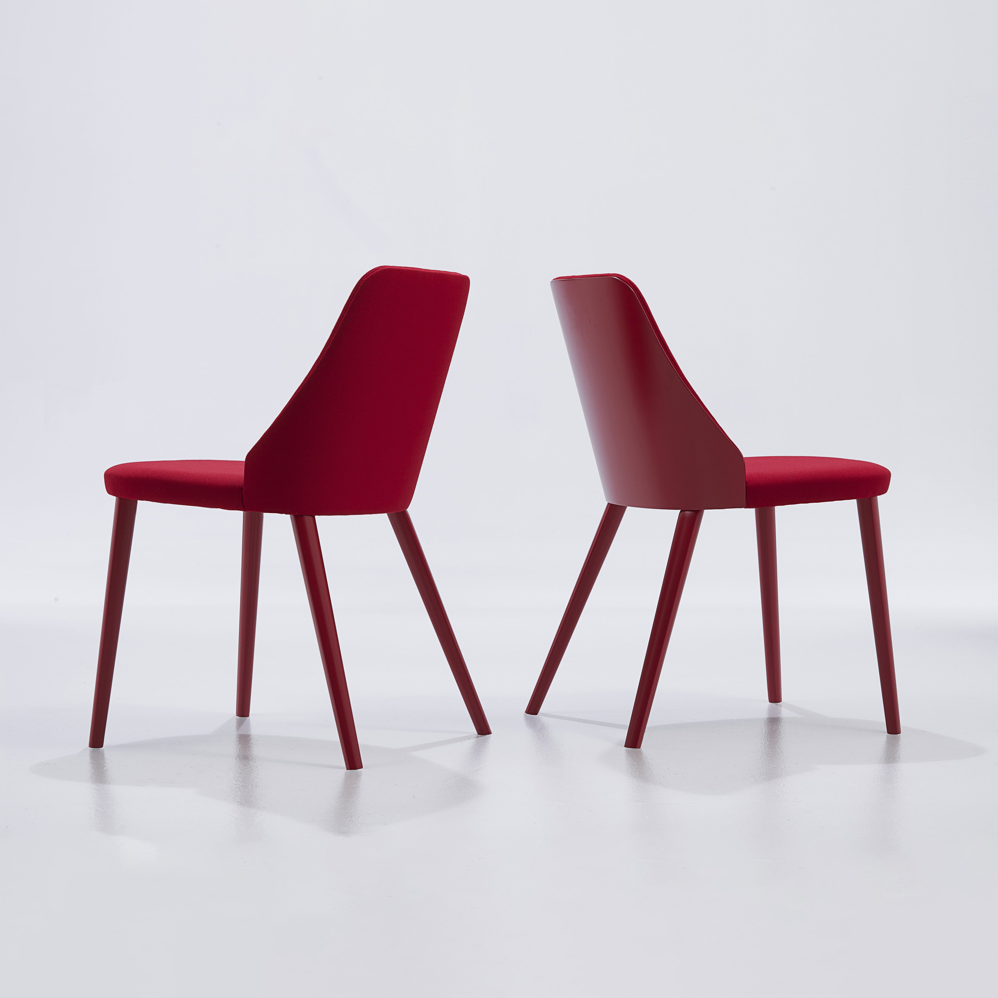 Two Break Dining Chairs in red upholstery shown from behind and at an angle, highlighting the sculptural shell and slim legs.
