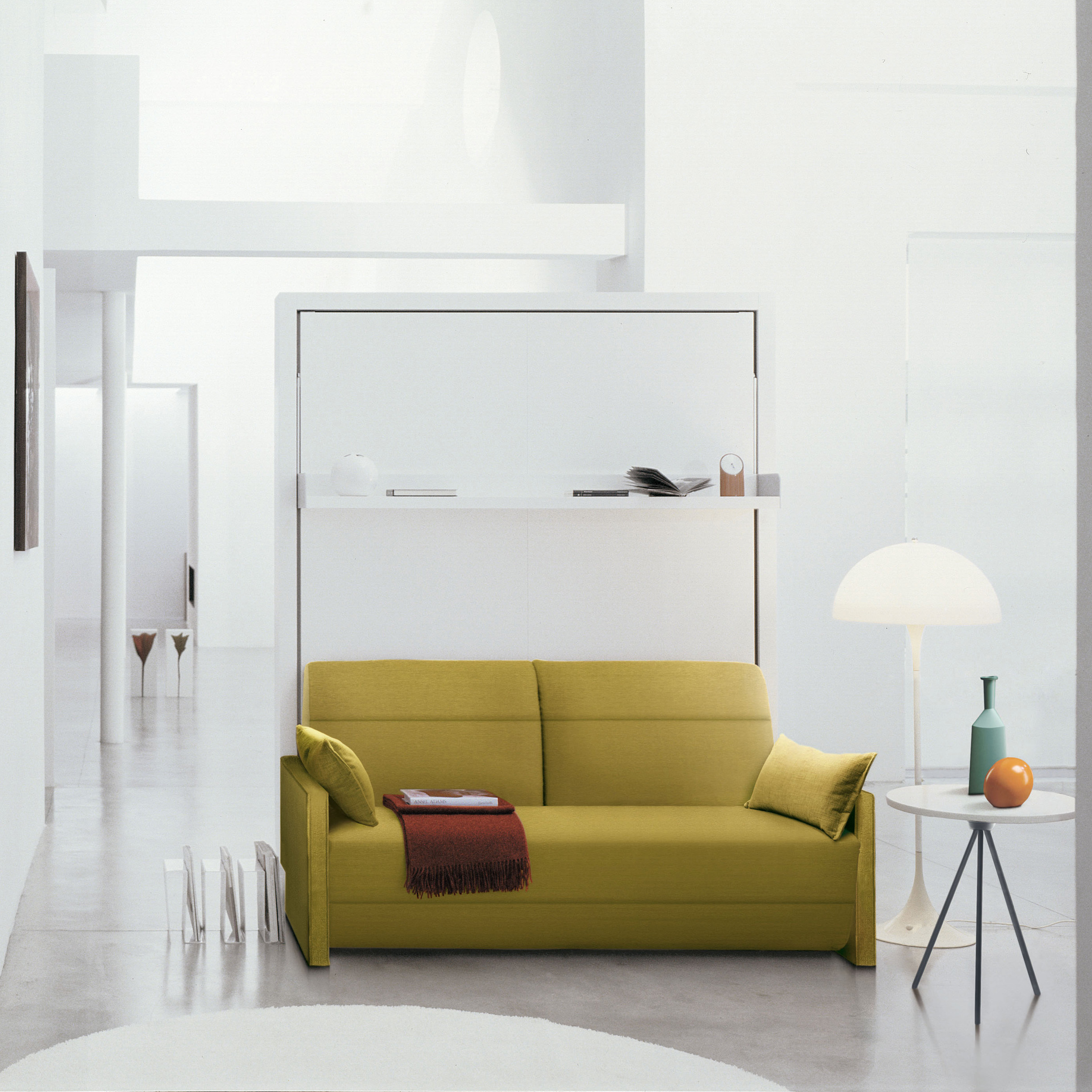Ito queen wall bed with reclining sofa in modern white interior, featuring a mustard yellow couch and integrated wall shelf.
