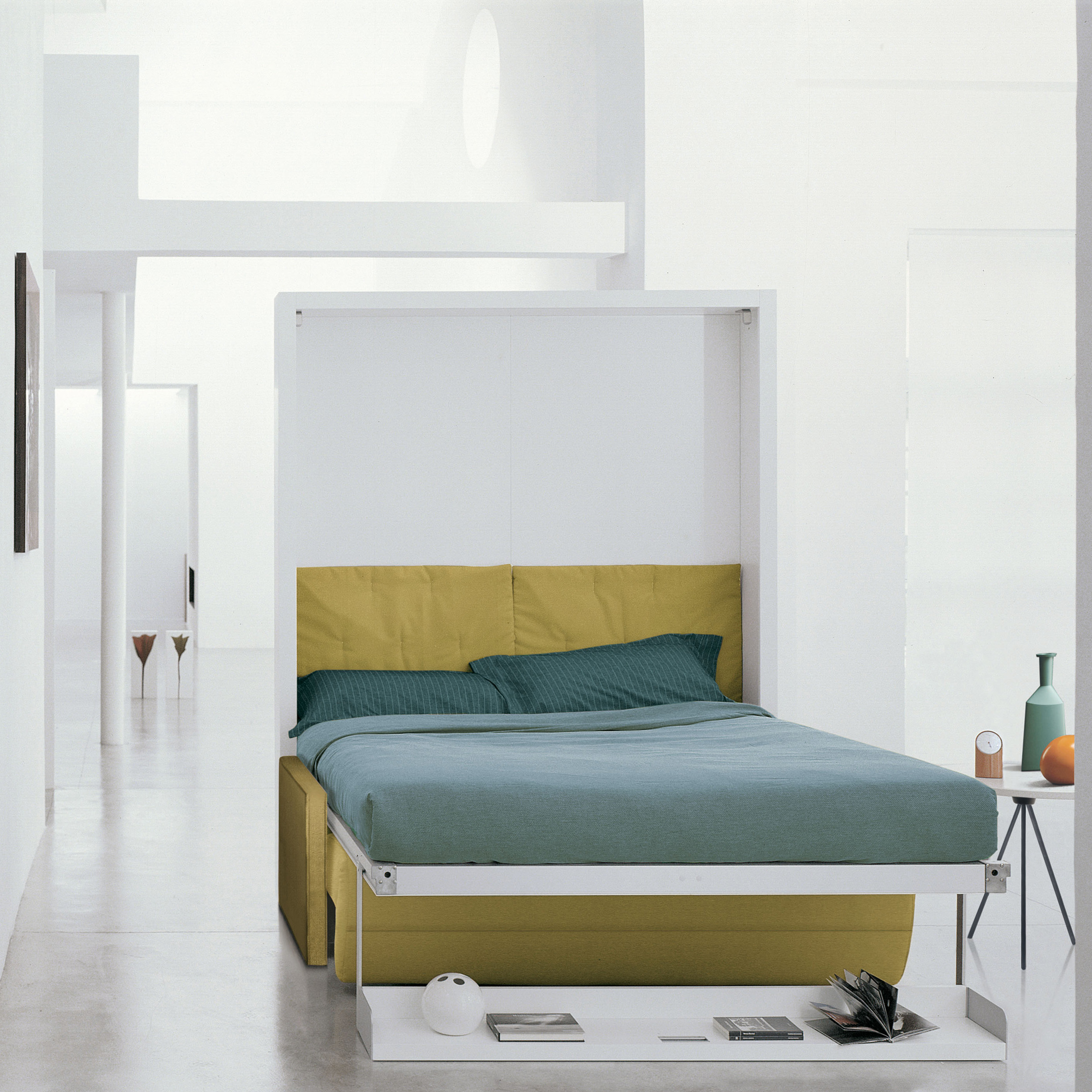 Ito queen wall bed with yellow reclining sofa, shown open to reveal a neatly made bed with teal bedding in a minimalist white interior.
