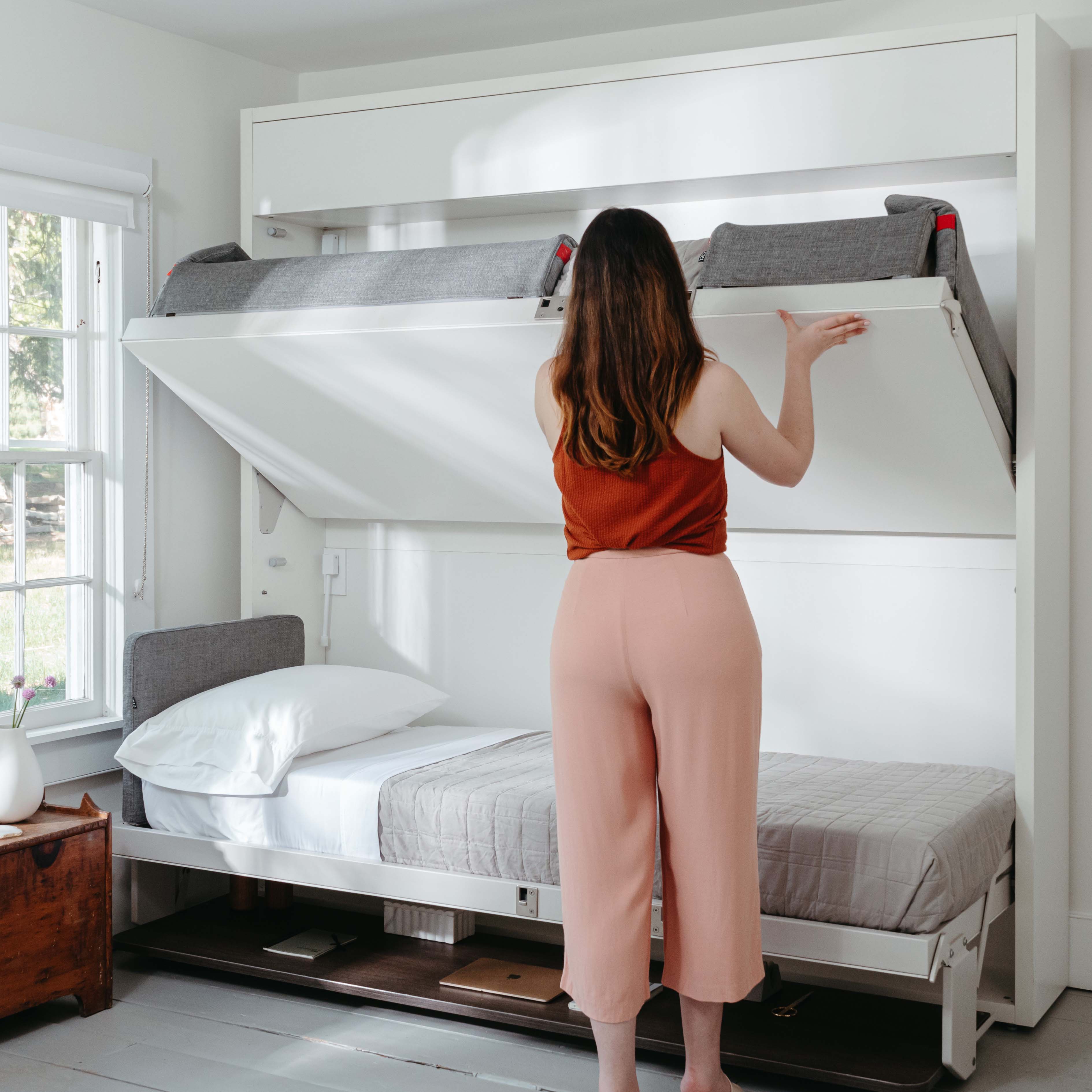 Woman stowing the Kali Duo Desk XL Twin Murphy bunk bed, a multifunctional space saving furniture solution with integrated desk.
