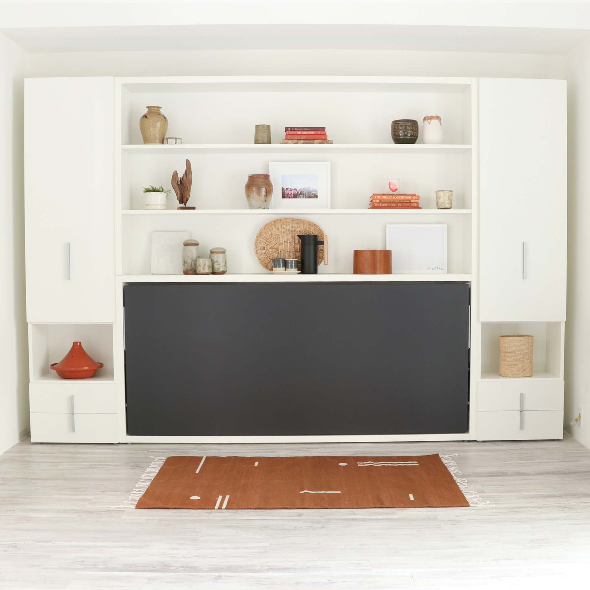 Kali horizontal twin Murphy bed in the closed position with dark front panel, built into a custom wall unit with open shelves and storage cabinets.