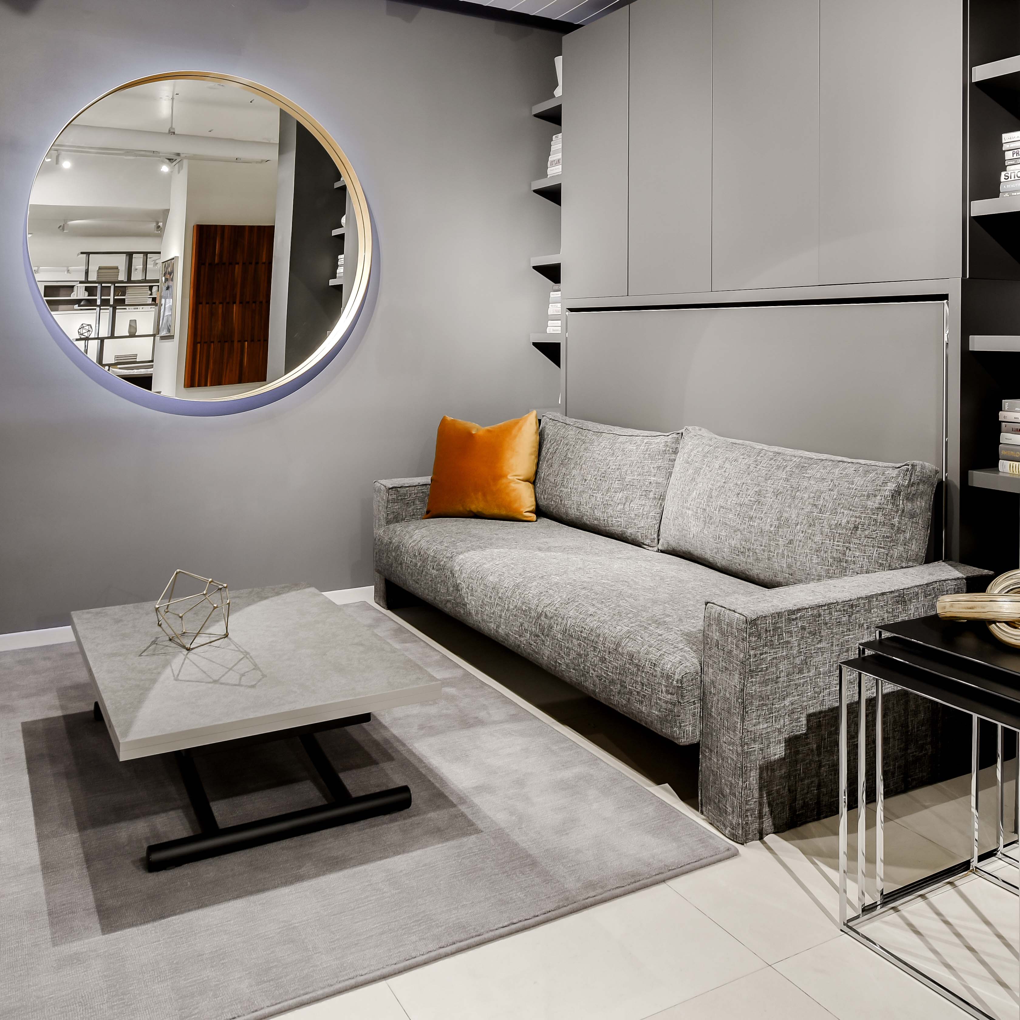 Murphy bed with couch in a contemporary gray living room with round mirror and minimalist decor.