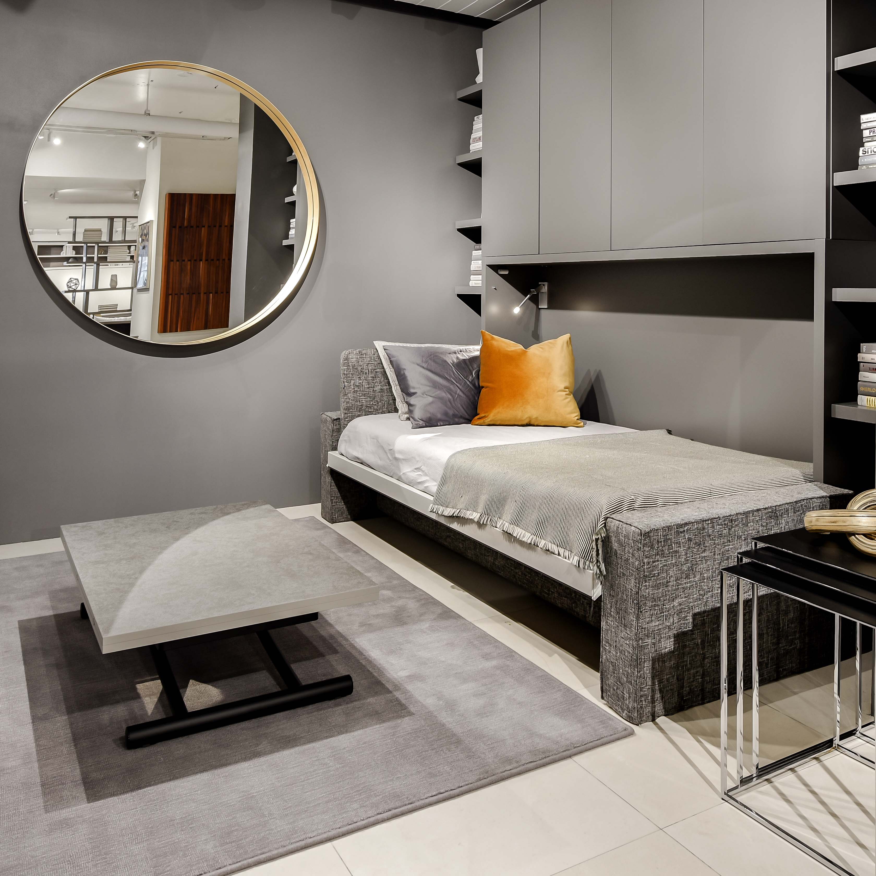 Murphy bed shown open in gray living room, revealing single bed with integrated sofa and overhead storage.