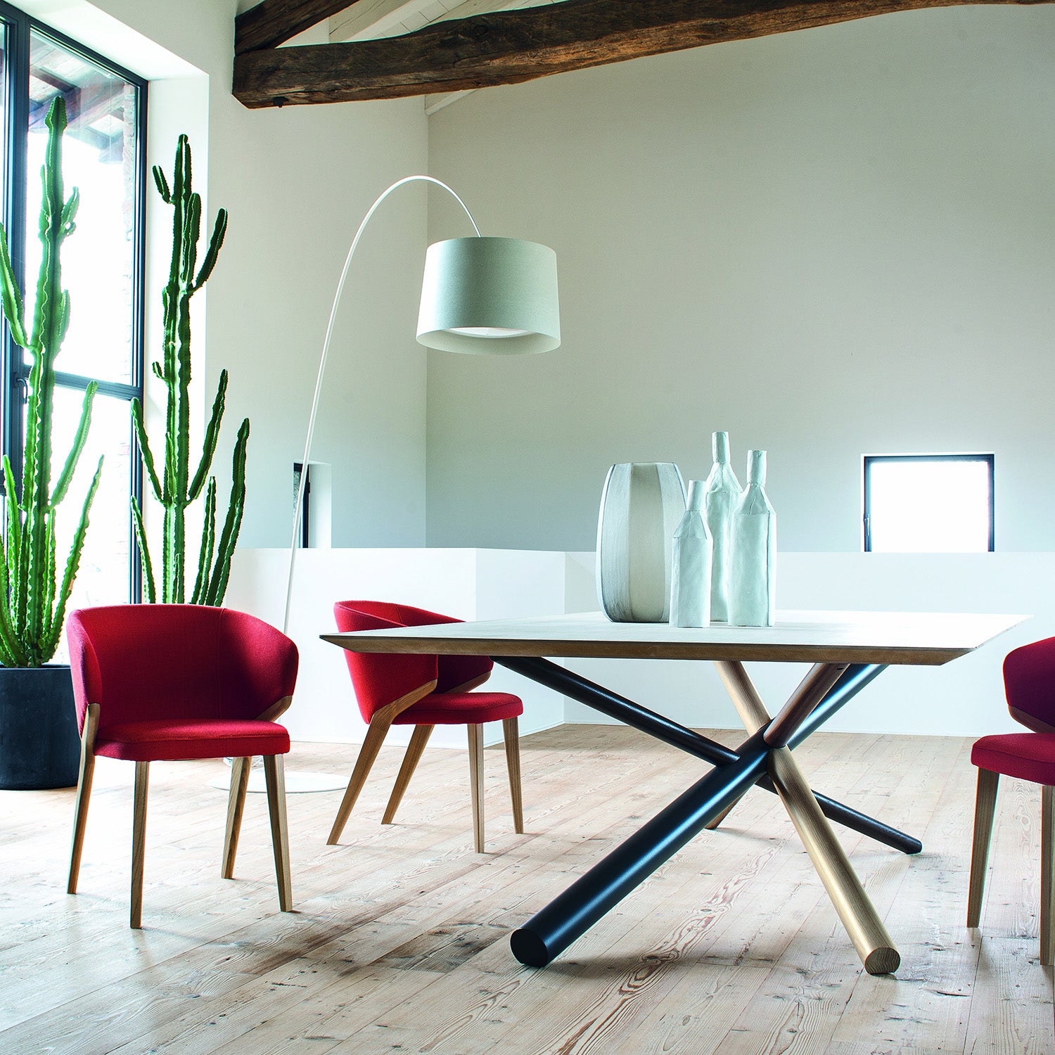 Set of Nora dining chairs in red upholstery around a contemporary dining table in a loft-style interior with wood flooring and large windows.