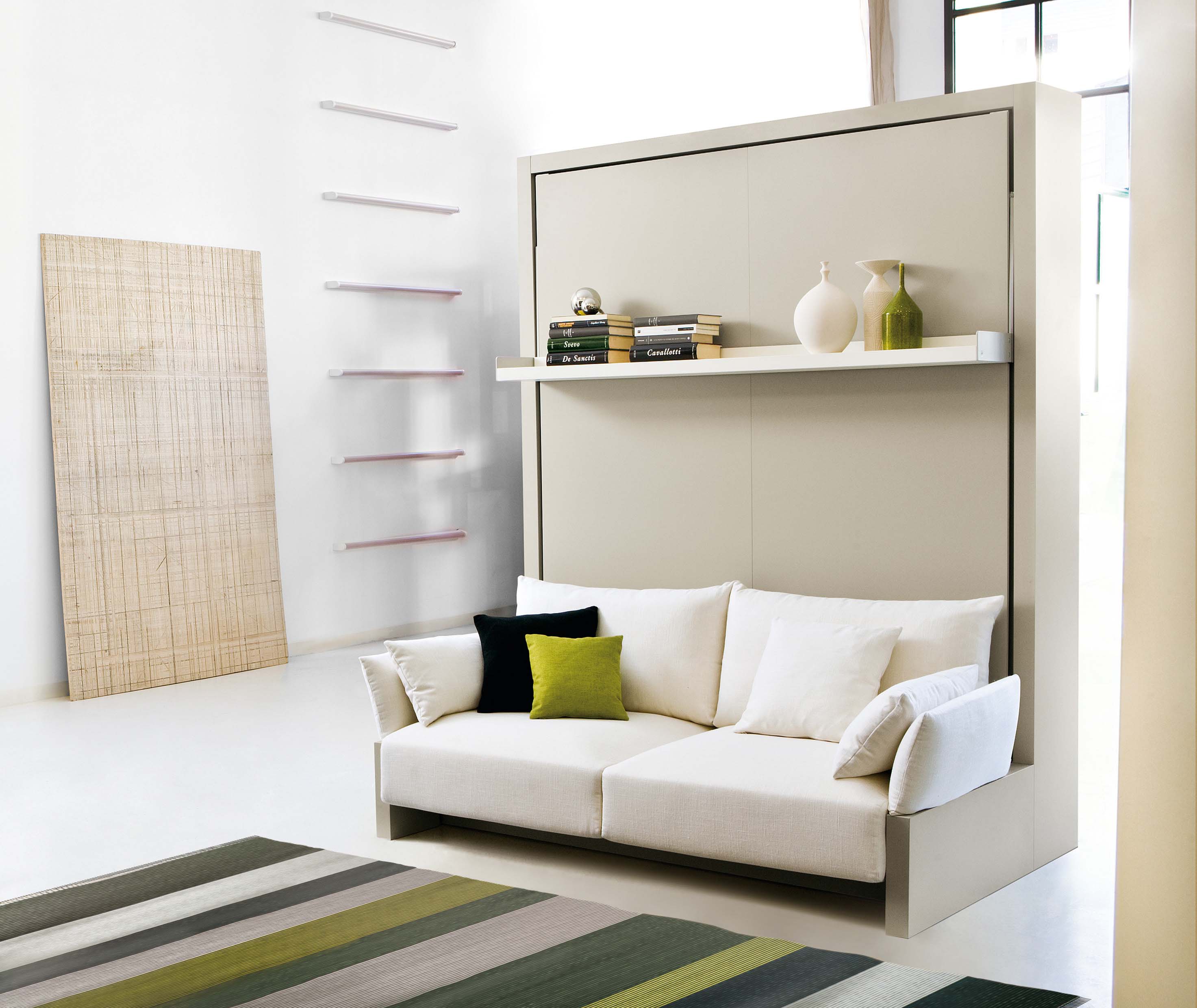 Nuovoliola wall bed in closed position with modern sofa and floating shelf, styled with books and decor.