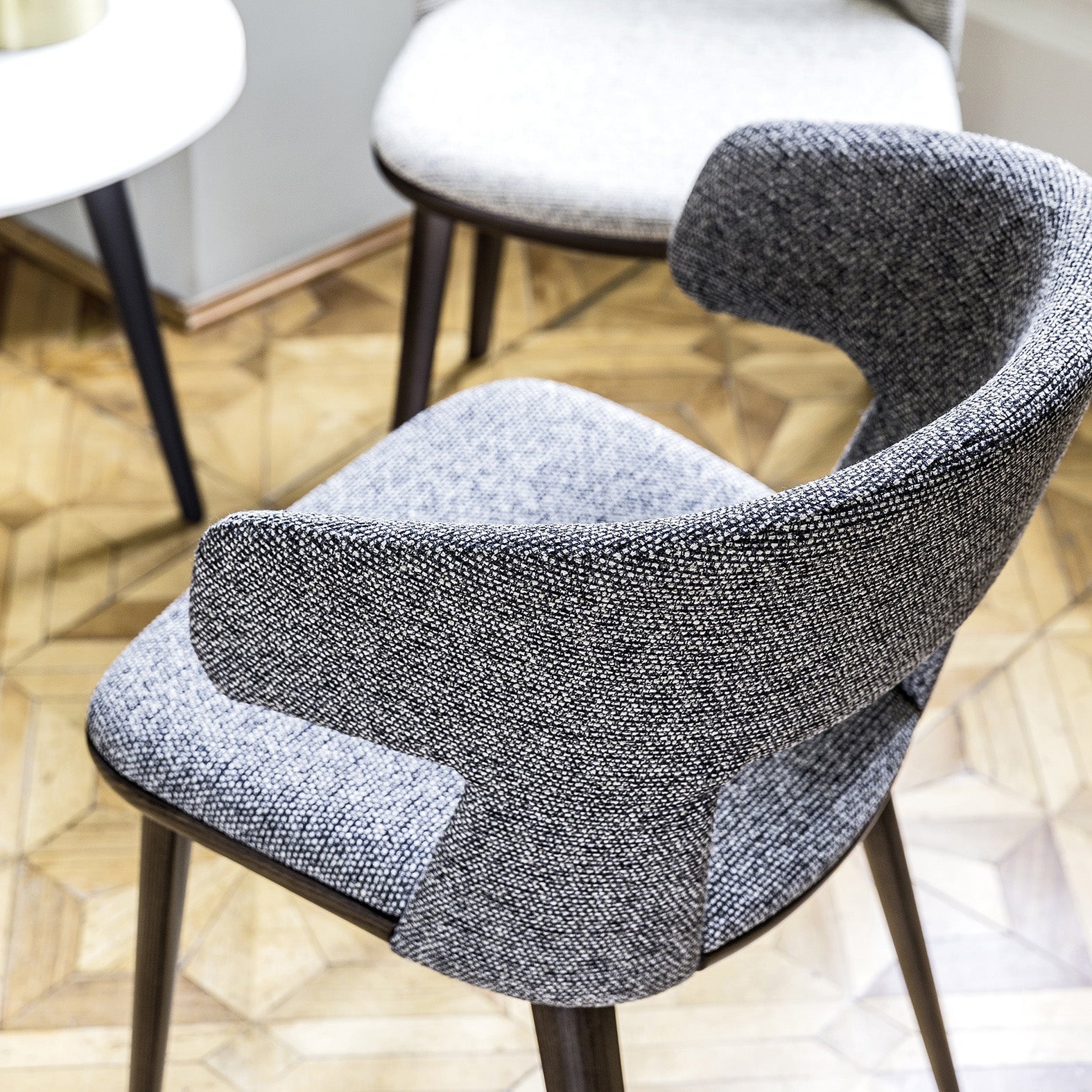 Close-up of Path armchair’s textured upholstery and open-back design, with dark wood frame and parquet flooring.