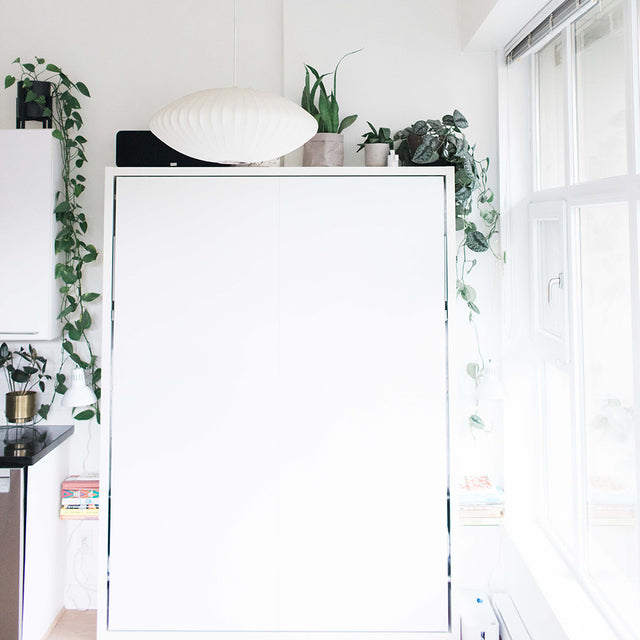 Queen Murphy bed with a white frame closed against a white wall in a modern kitchen interior.
