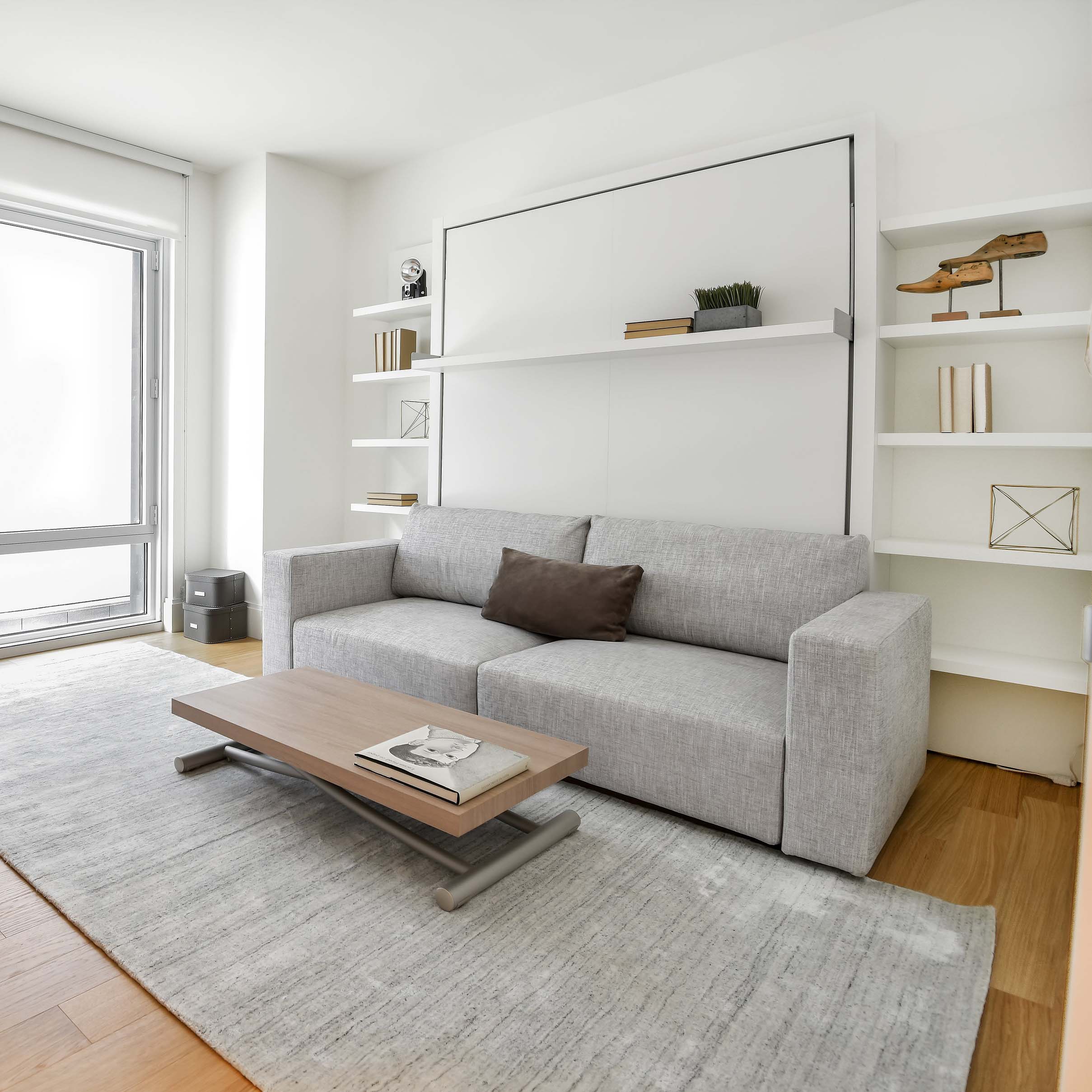 Swing 0 Murphy bed closed with light gray upholstered sofa and wall-mounted shelf in bright, modern room.