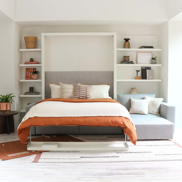 Swing Chaise Murphy bed shown fully opened with bedding, integrated into a contemporary wall unit with light gray sectional sofa.