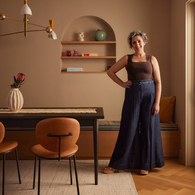 Interior designer Isabella Patrick standing in a modern Cobble Hill dining room featuring warm neutral tones, brass light fixture, and leather dining chairs.