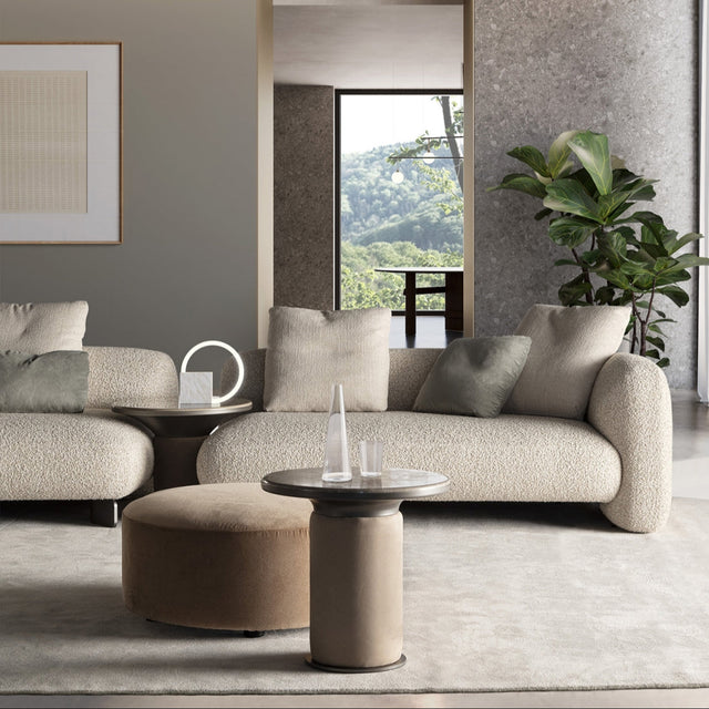 Modern living room with beige Bobbin side table, curved upholstered sofas, neutral throw pillows, and large windows showcasing a scenic view.