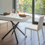 Brooklyn Mini table extended to dining height, set for two with white chairs, against a backdrop of greenery and modern decor.