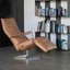 Cascade modern recliner in caramel leather with a sleek chrome base, positioned in a contemporary living room with a bookshelf in the background.