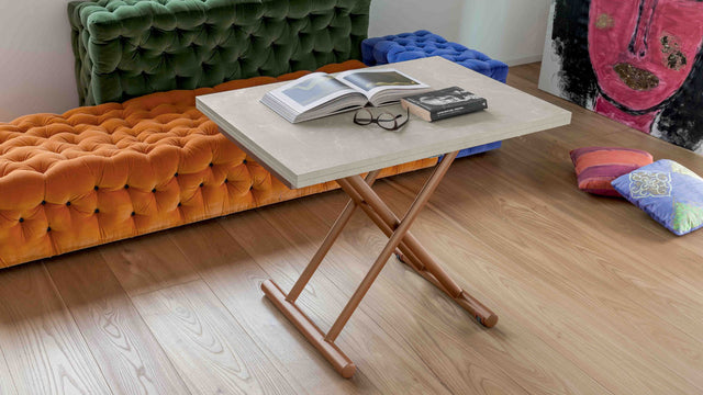 Doppio Long transforming table in its closed configuration, styled with a beige ceramic top and bronze base, in a vibrant living room with orange tufted seating.