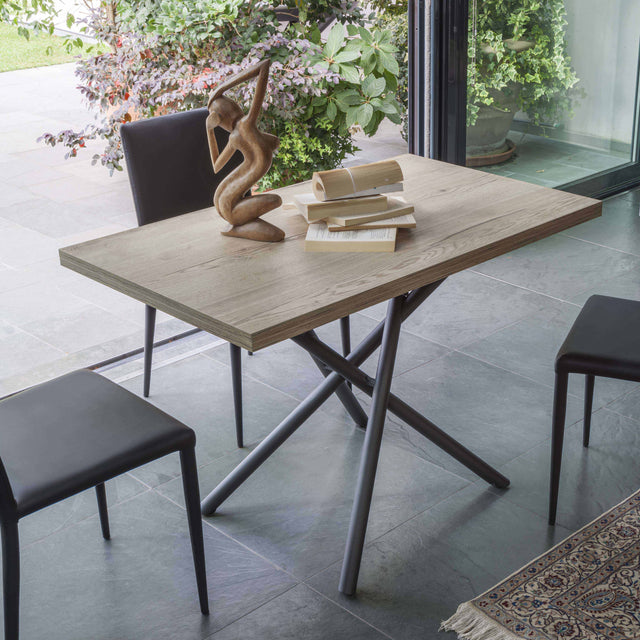 The Rotasu transforming table in its dining table configuration, paired with three modern black chairs, surrounded by a light-filled indoor-outdoor setting.