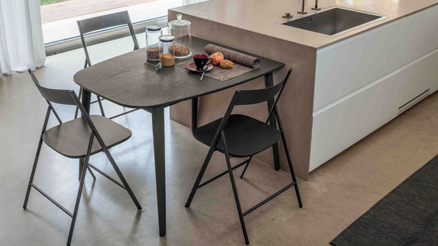 Surf table in wood veneer finish set as a compact breakfast table for three, styled with a modern kitchen island and black folding chairs.