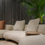Detail view of the Kintai modular sofa showing soft curves, neutral fabric, and accent pillows beside greenery in a modern living room.