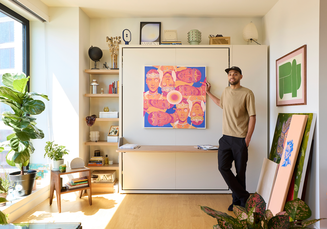 Josh Ayala standing beside his closed Penelope Desk wall bed with built-in desk and bold artwork in his NYC studio, photographed by Erin Derby