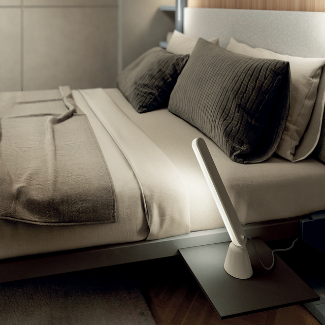 Close-up of an LGM Murphy bed (Resource Furniture) showing beige linen bedding, gray textured pillows and a gray upholstered headboard with a modern bedside lamp on an integrated shelf — space-saving bedroom furniture.