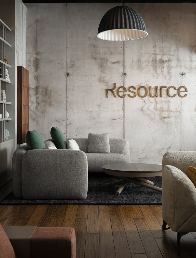 Resource Furniture Seattle showroom — modern lounge with gray curved sofas, green pillows, round wood coffee table and concrete accent wall. Photography by Anton Benedikt.