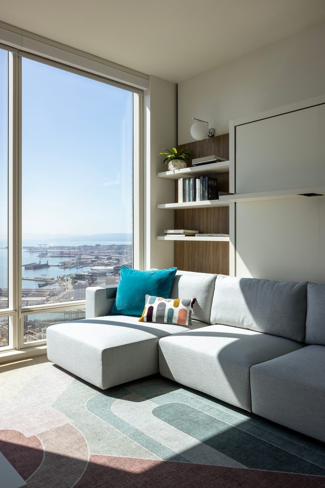 Resource Furniture Swing Sectional queen Murphy bed with couch, open position in a bright bay-view guest room with built-in shelving.