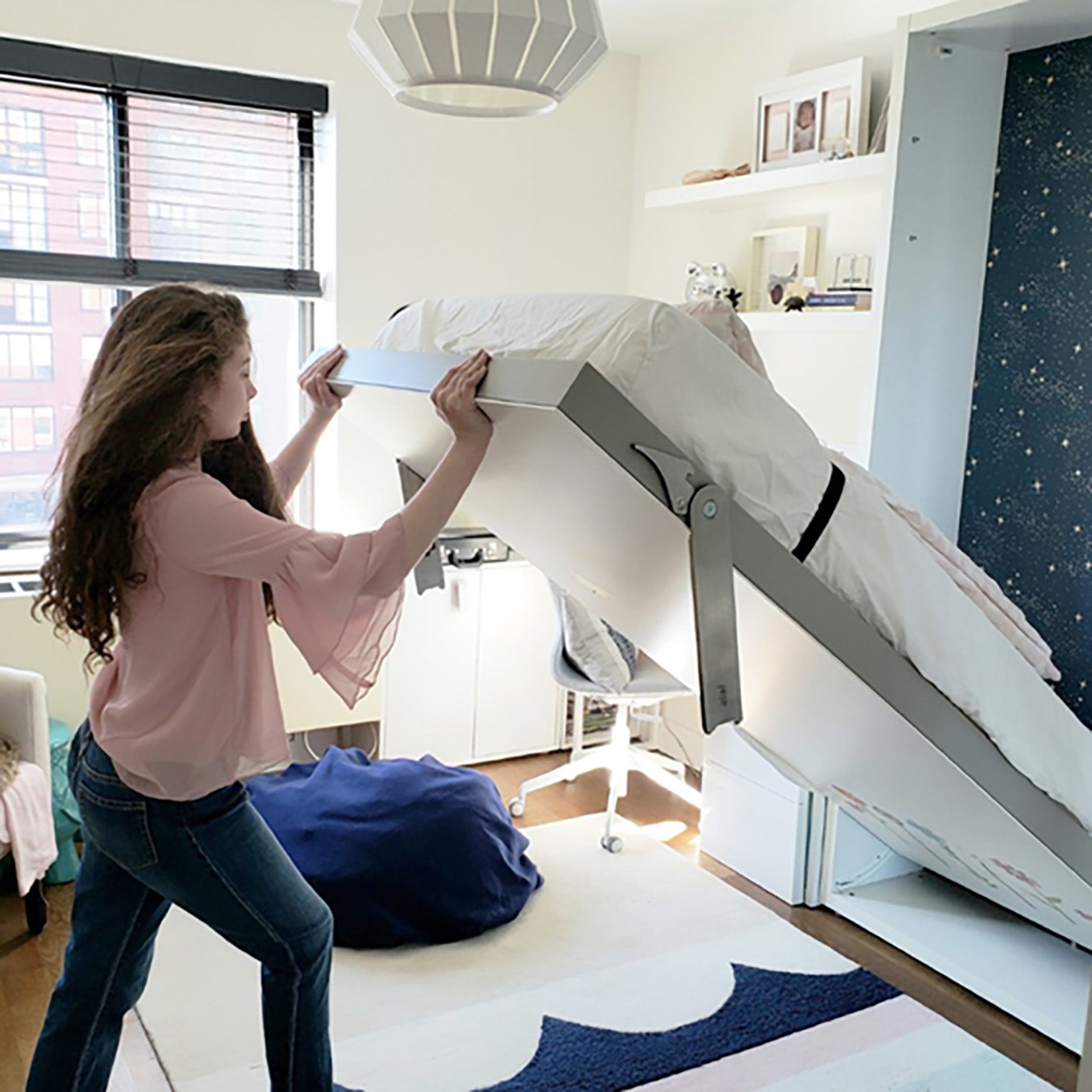 Girl folding up the Altea Twin Murphy bed into the wall, showcasing space saving furniture for small bedrooms.