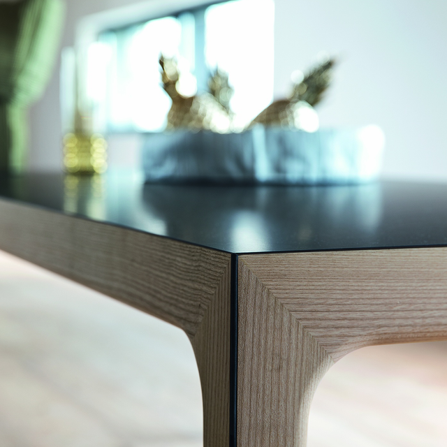 Close-up of Amalong dining table corner in natural ash with black top, styled with gold pineapples and sculptural decor.