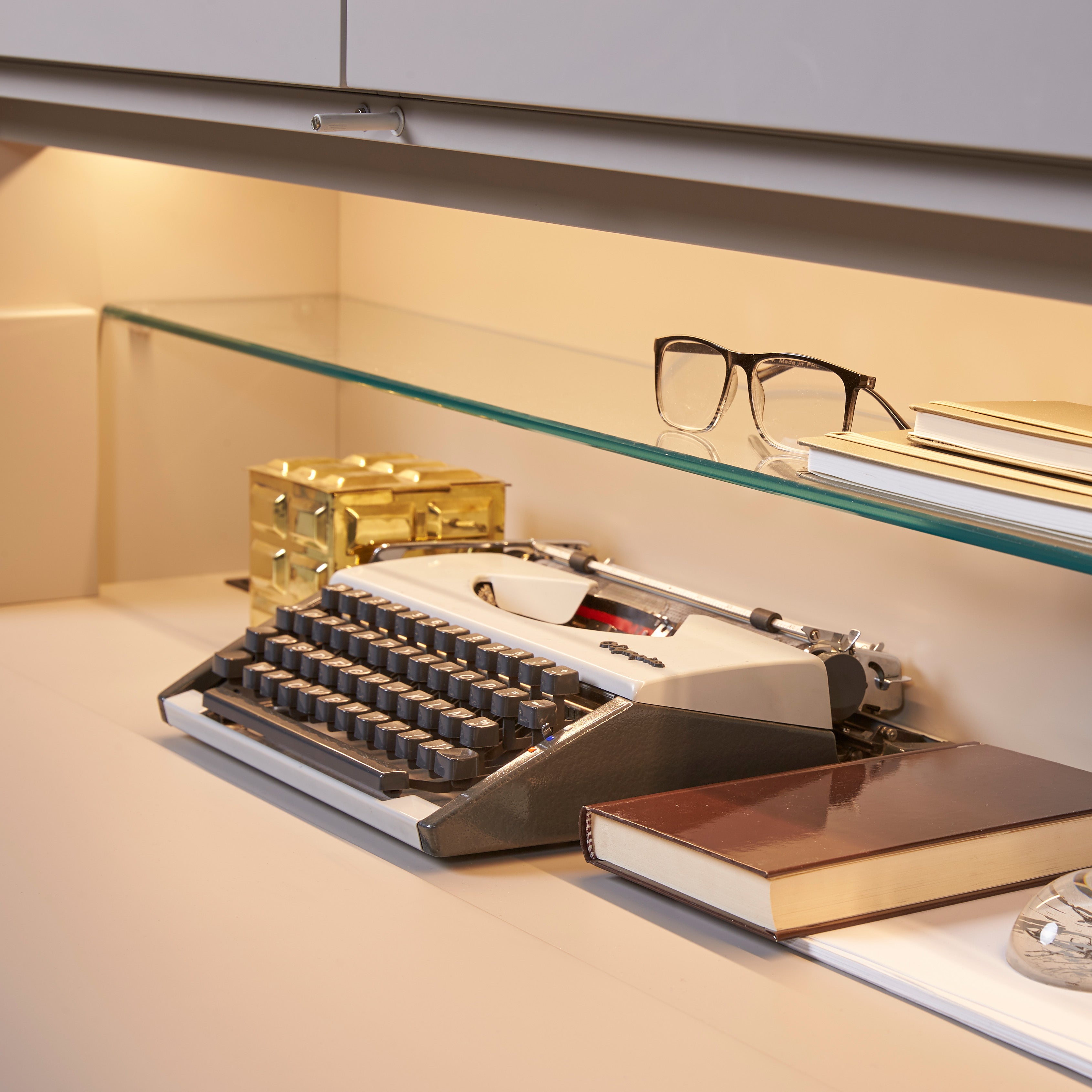 Custom cabinetry units desk shelf detail with typewriter, books, and glass shelf — modern space-saving furniture by Resource Furniture.