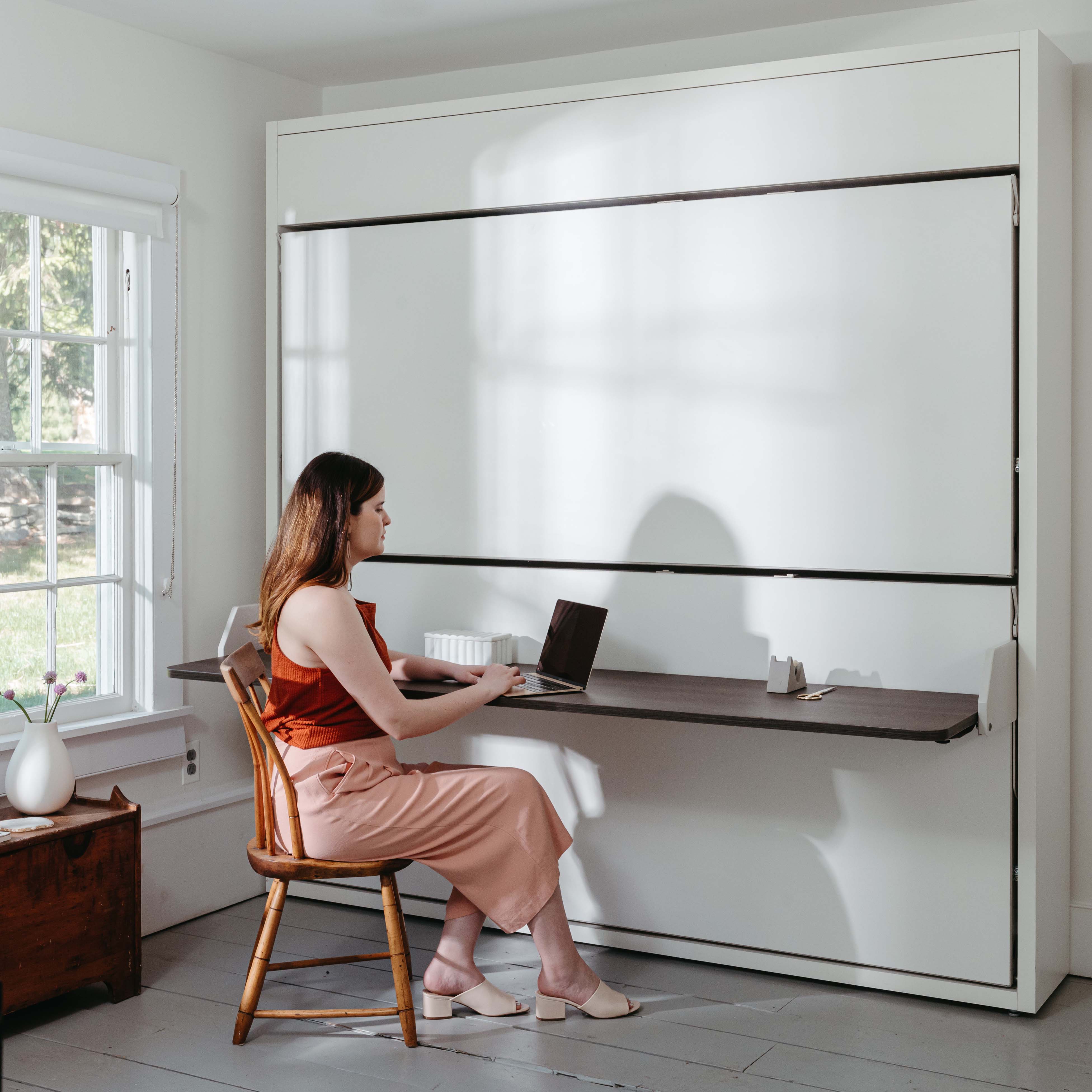 Woman working at the integrated desk of the Kali Duo Desk XL Twin Murphy bunk bed, a multifunctional space saving furniture solution for small rooms.