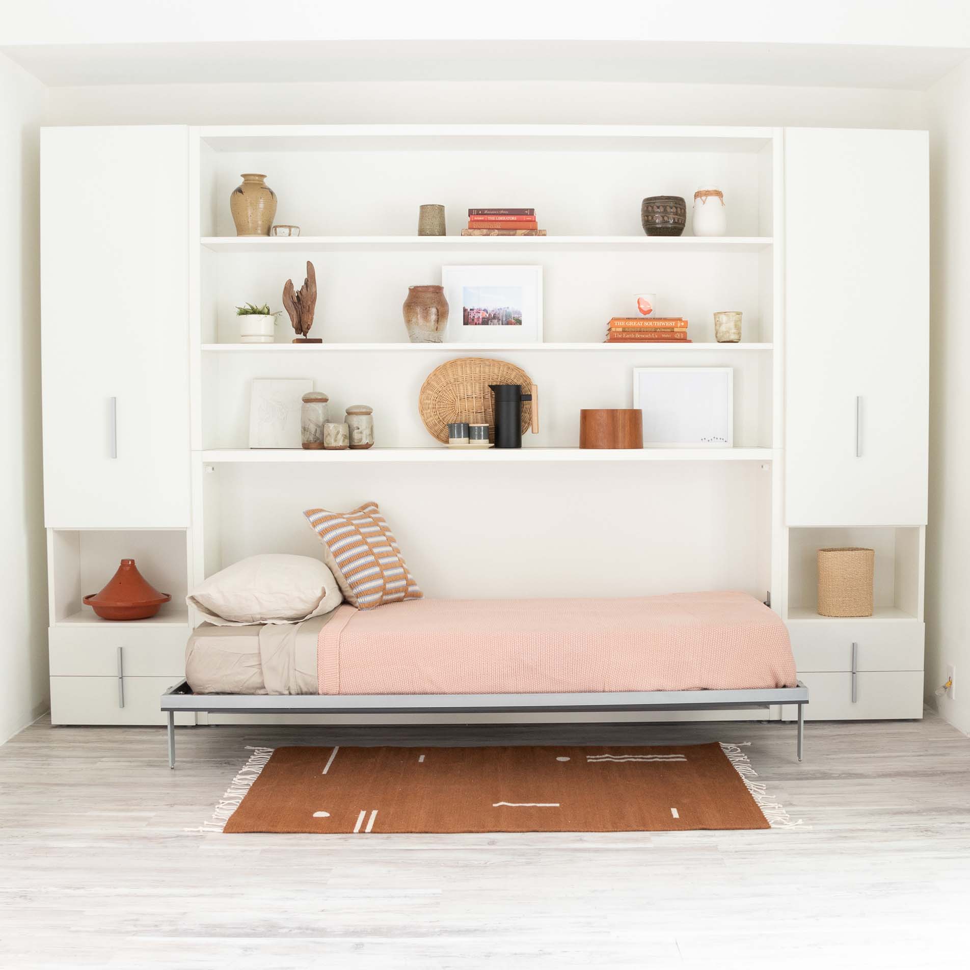 Kali horizontal twin Murphy bed shown open with bedding, integrated into a sleek white shelving and cabinet system in a modern interior.